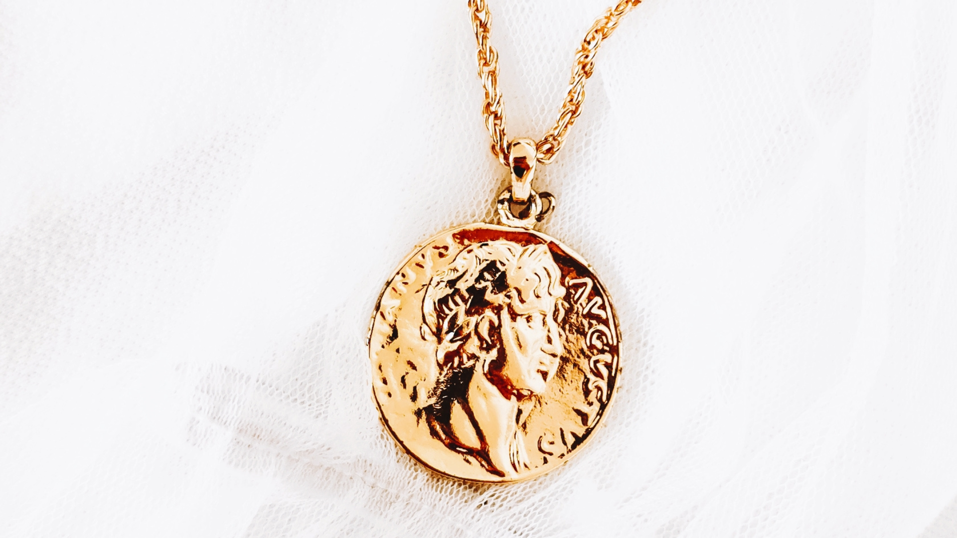 A gold necklace with a coin pendant on a chain.