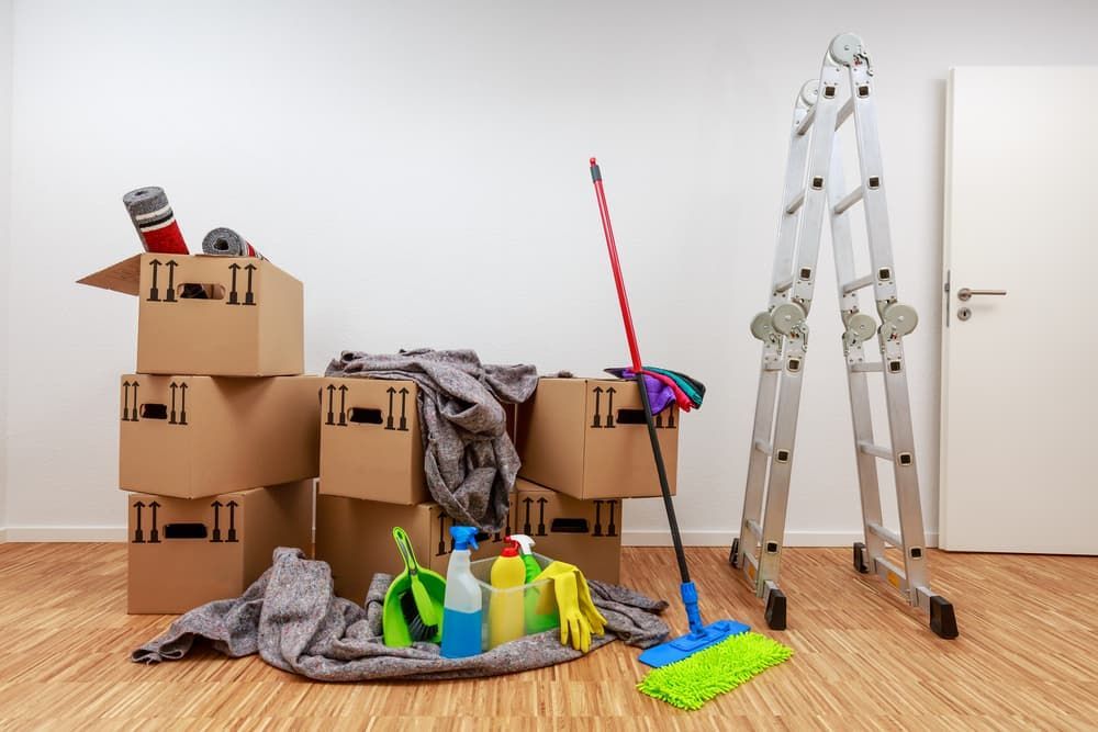 Cardboard boxes, cleaning supplies, and a ladder in an empty room, possibly for moving or cleaning.