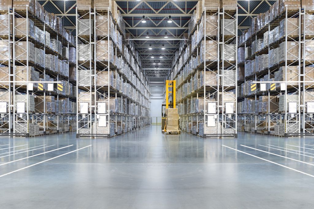 Warehouse interior with tall shelving packed with boxes; a forklift moves in the aisle.