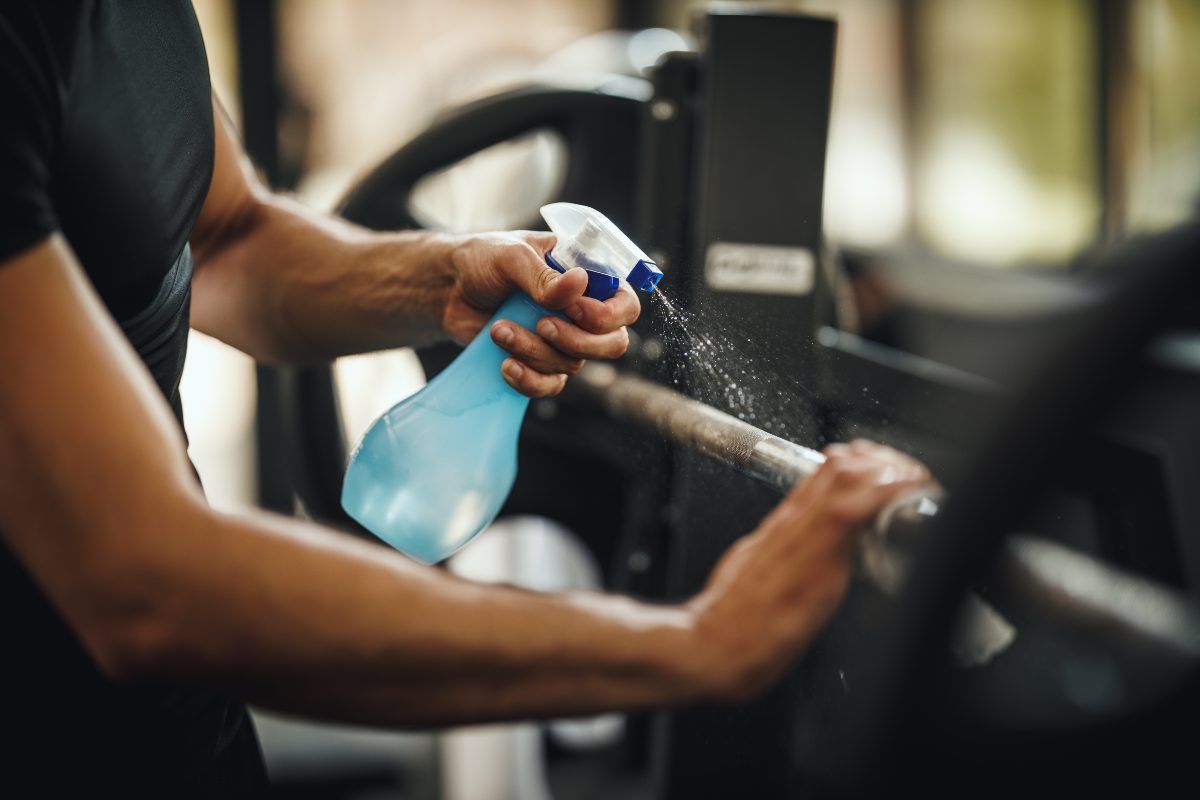 Person spraying disinfectant on gym equipment.