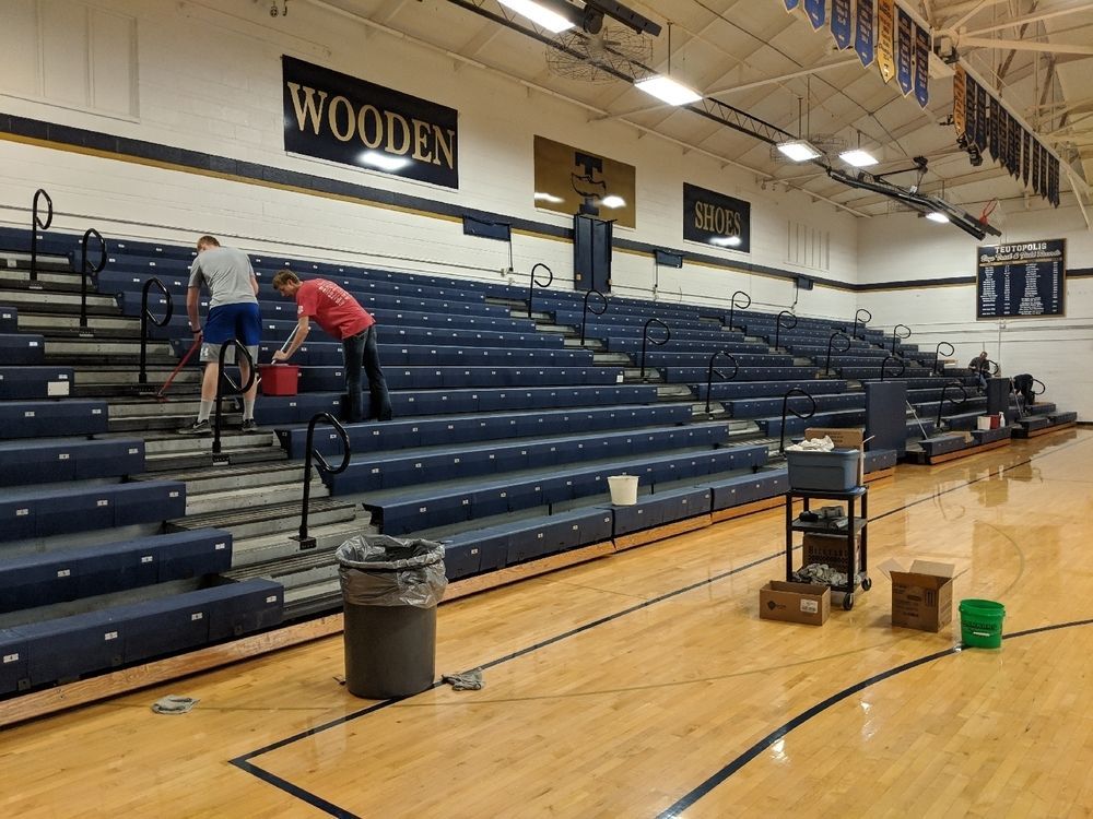 Two people cleaning bleachers in a gymnasium; 