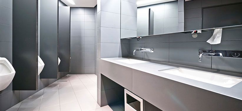 Modern public restroom with gray walls, stalls, and a long counter with sinks and a mirror.