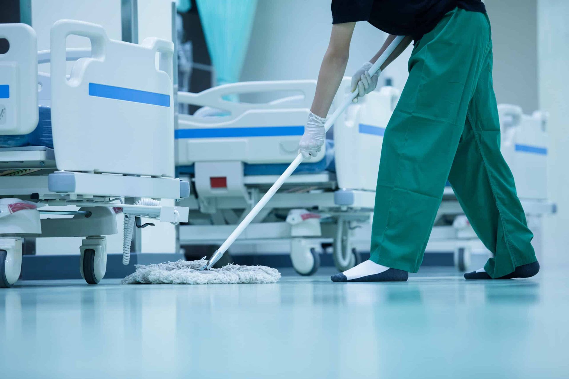 Person mopping a hospital floor between patient beds.