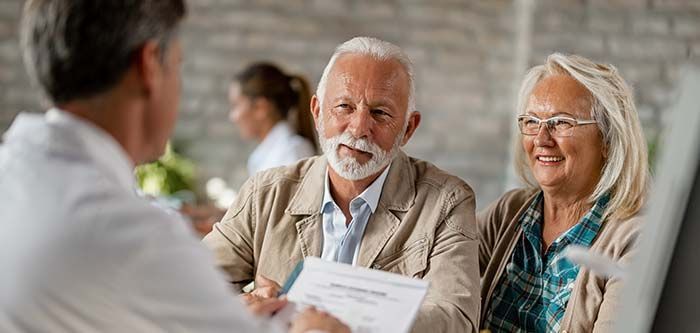 A doctor showing paperwork to an elderly couple in a medical office. They are smiling.