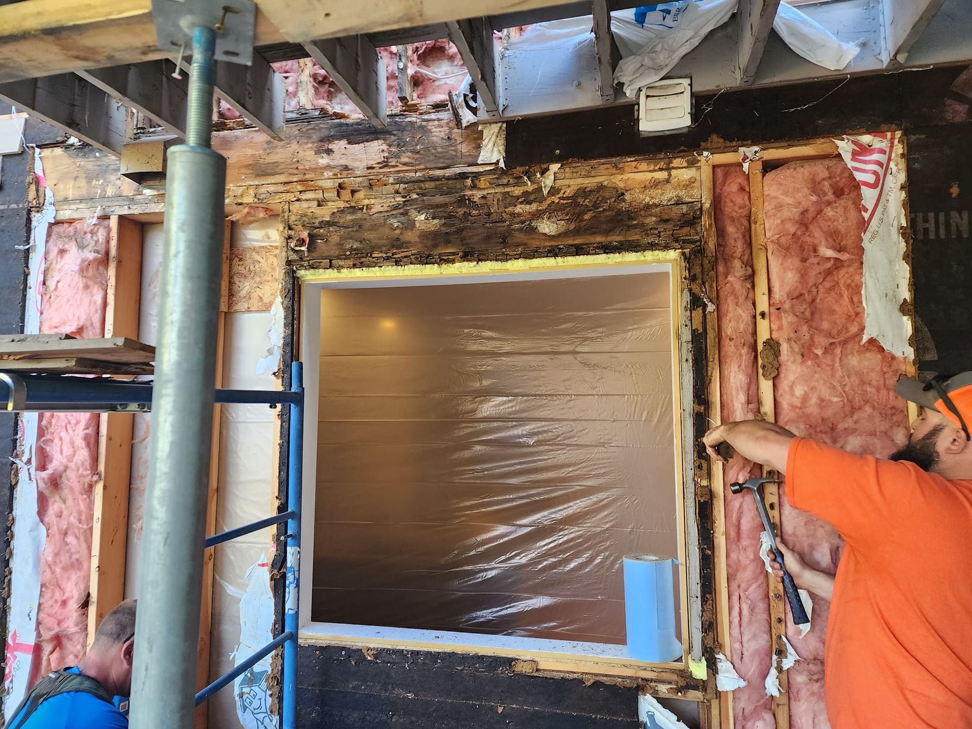 Construction workers near window, removing damaged wood siding, insulation, and framing.