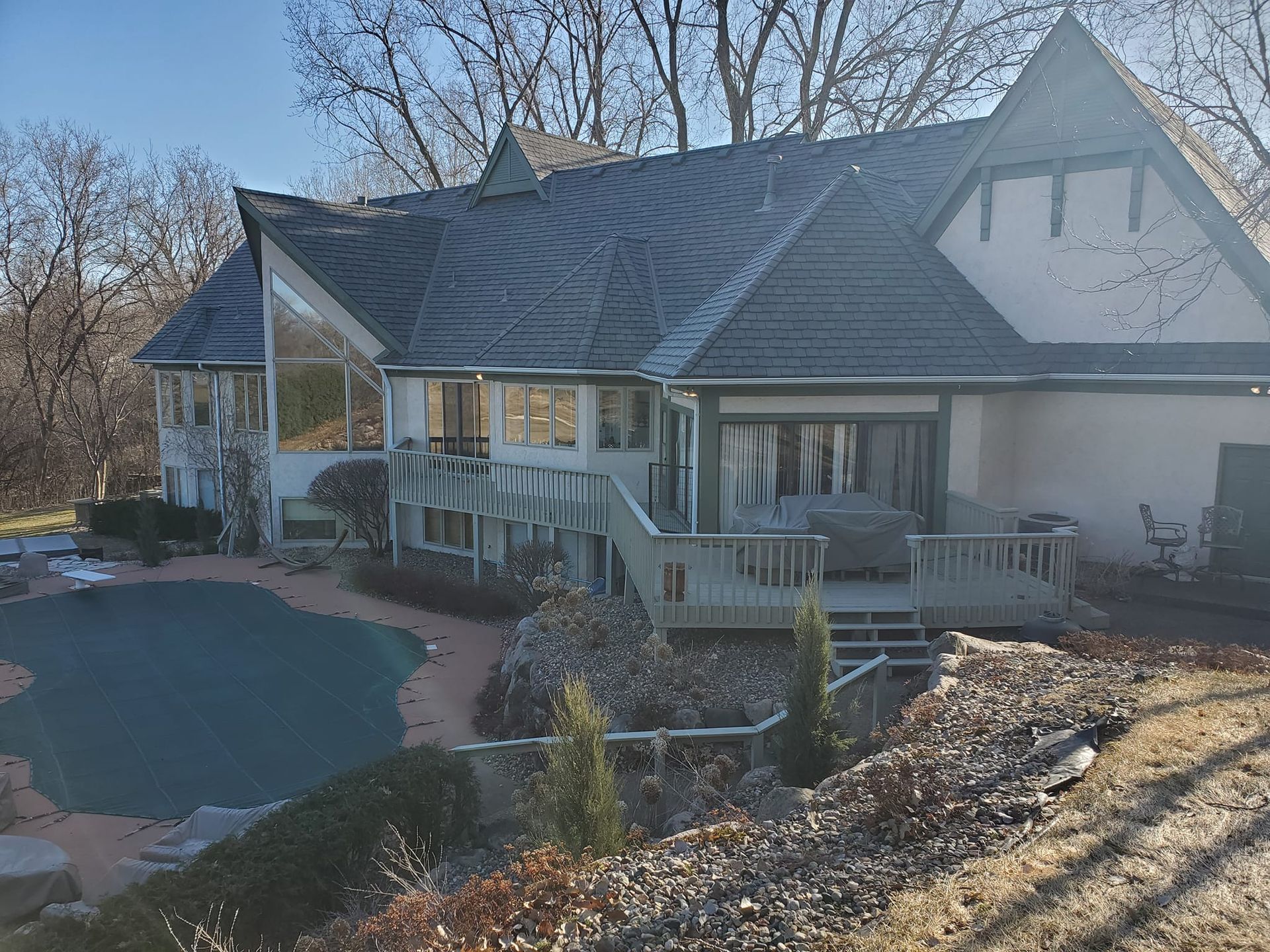 House with a dark roof and large windows, next to a pool and deck. The house is cream colored, with greenery in the yard.