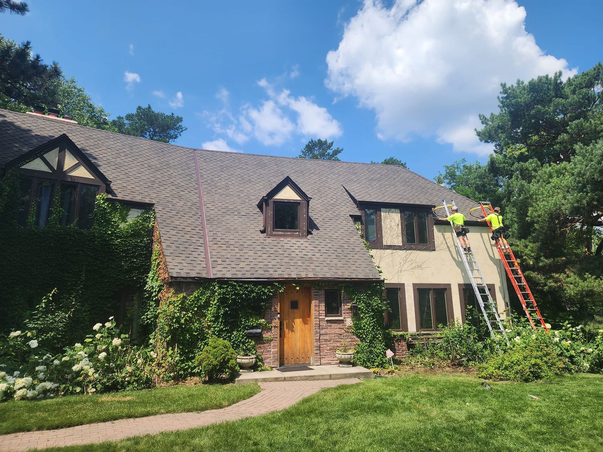House exterior with workers on ladders; roof repair under blue sky.