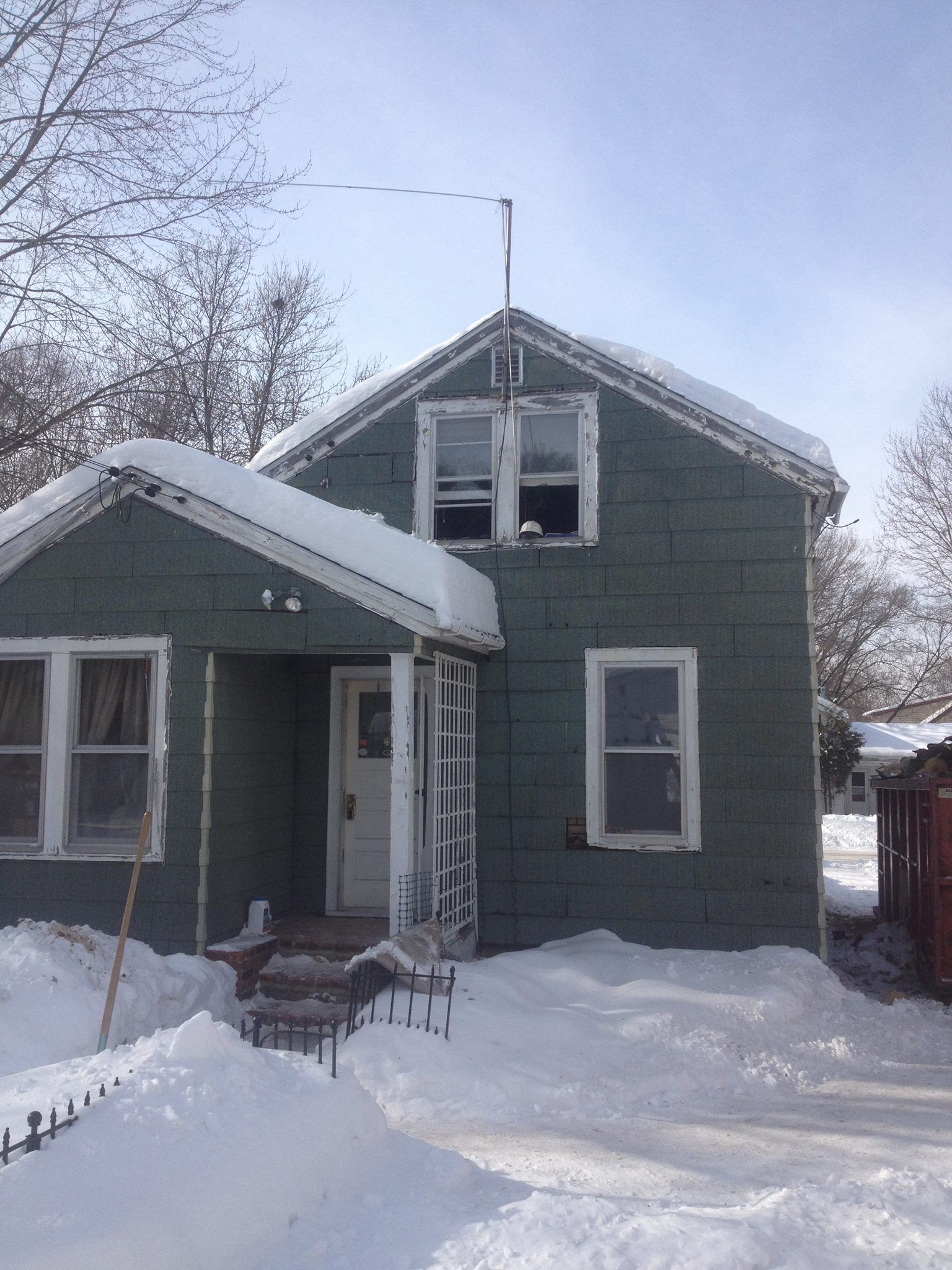 A small, teal-green house covered in snow with a front door and several windows.