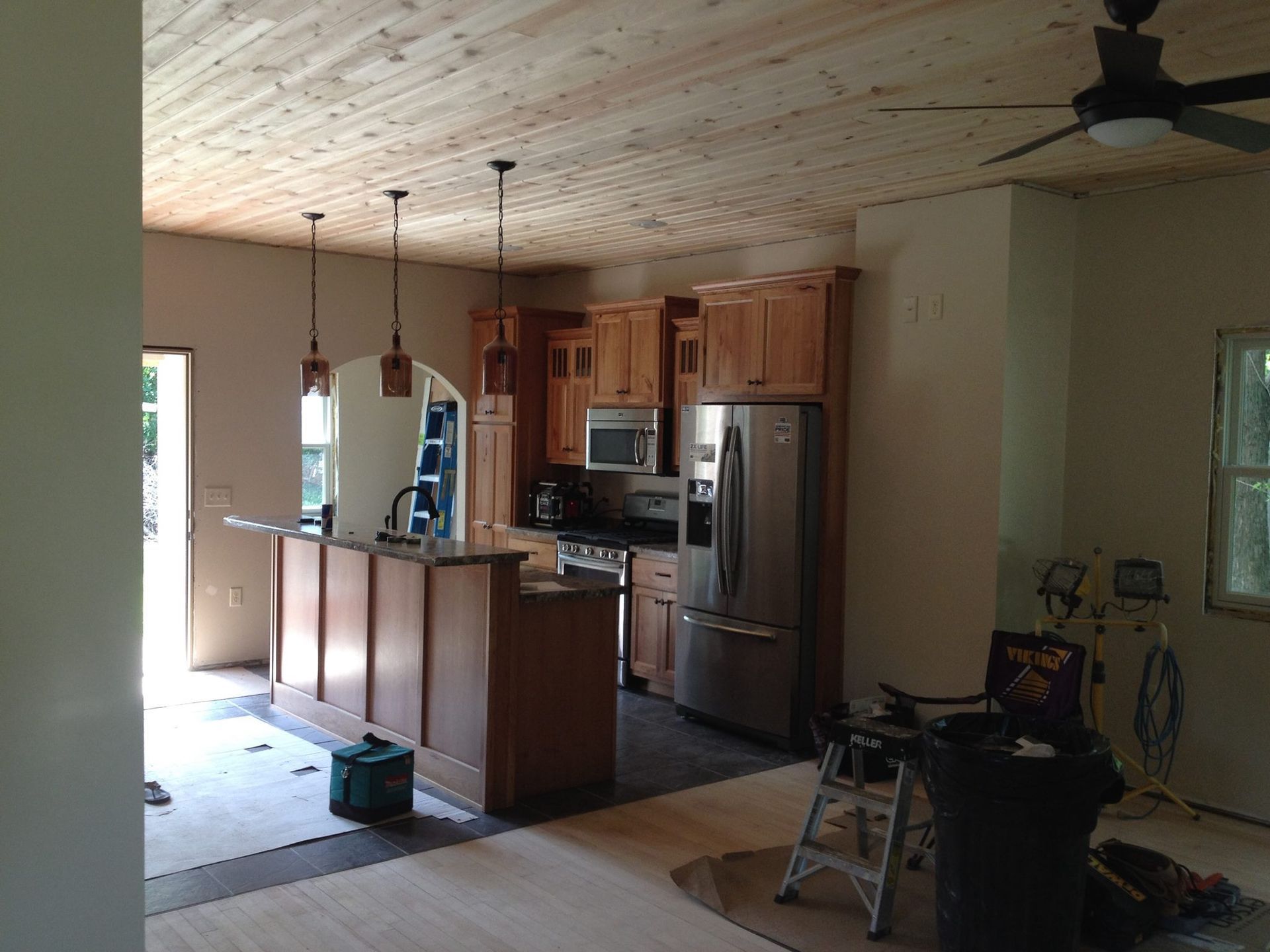 Kitchen under construction with wood cabinets, ceiling, and island. Stainless steel appliances and a view to the outside.