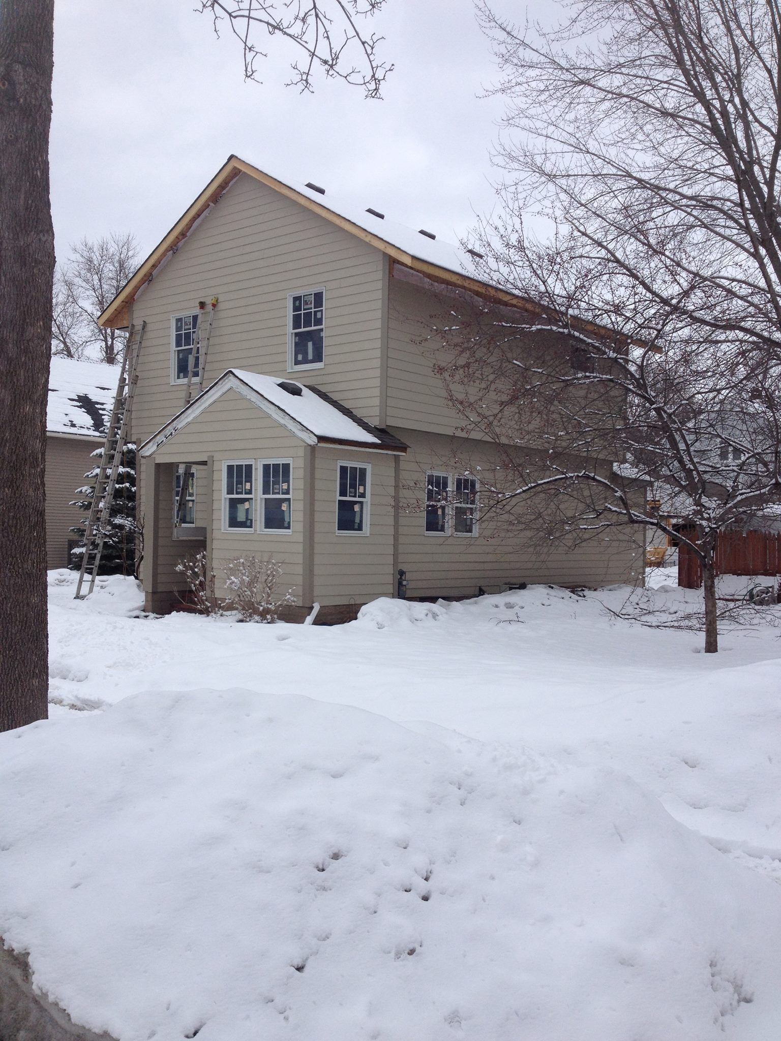 Two-story beige house with snow-covered yard and bare trees.