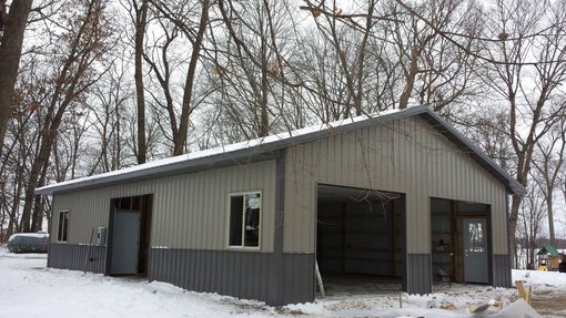 Metal garage building with gray and silver siding, snowy ground, and bare trees.