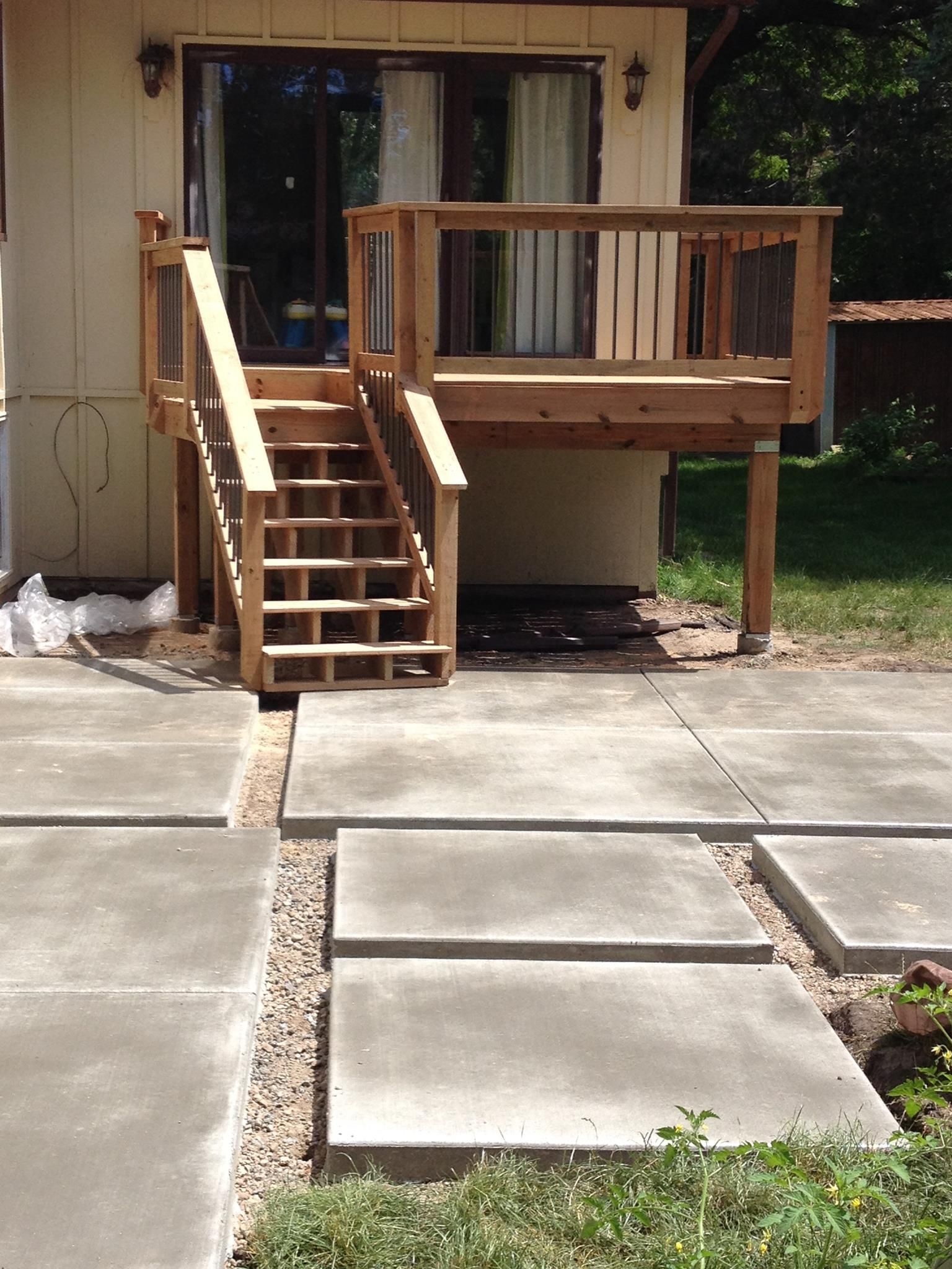 Wooden deck with stairs leading down to a concrete patio. Gravel pathway between concrete squares.