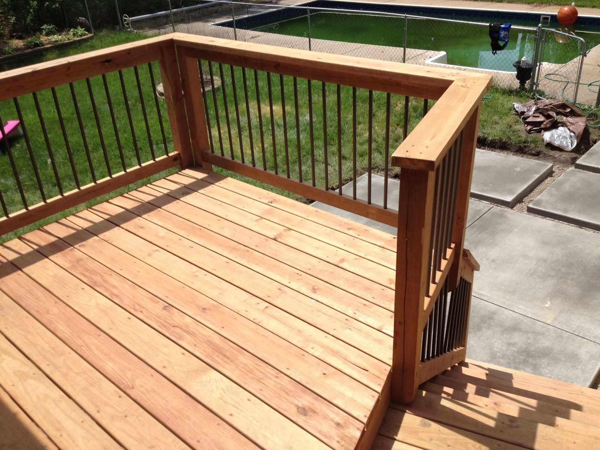 Wooden deck with black railings overlooking a green lawn and pool.