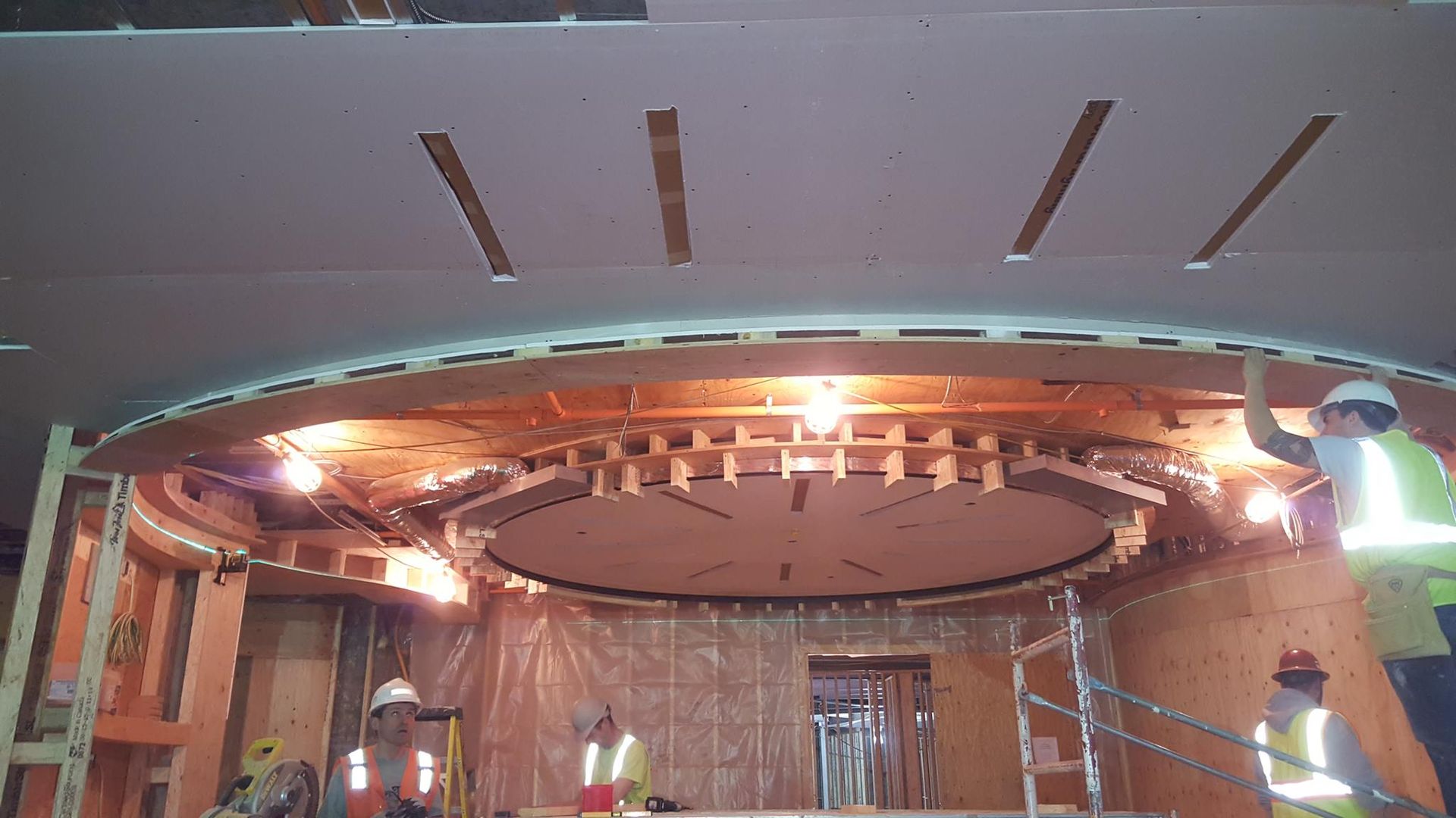 Construction in progress. Workers install a circular wooden structure within a building's interior.