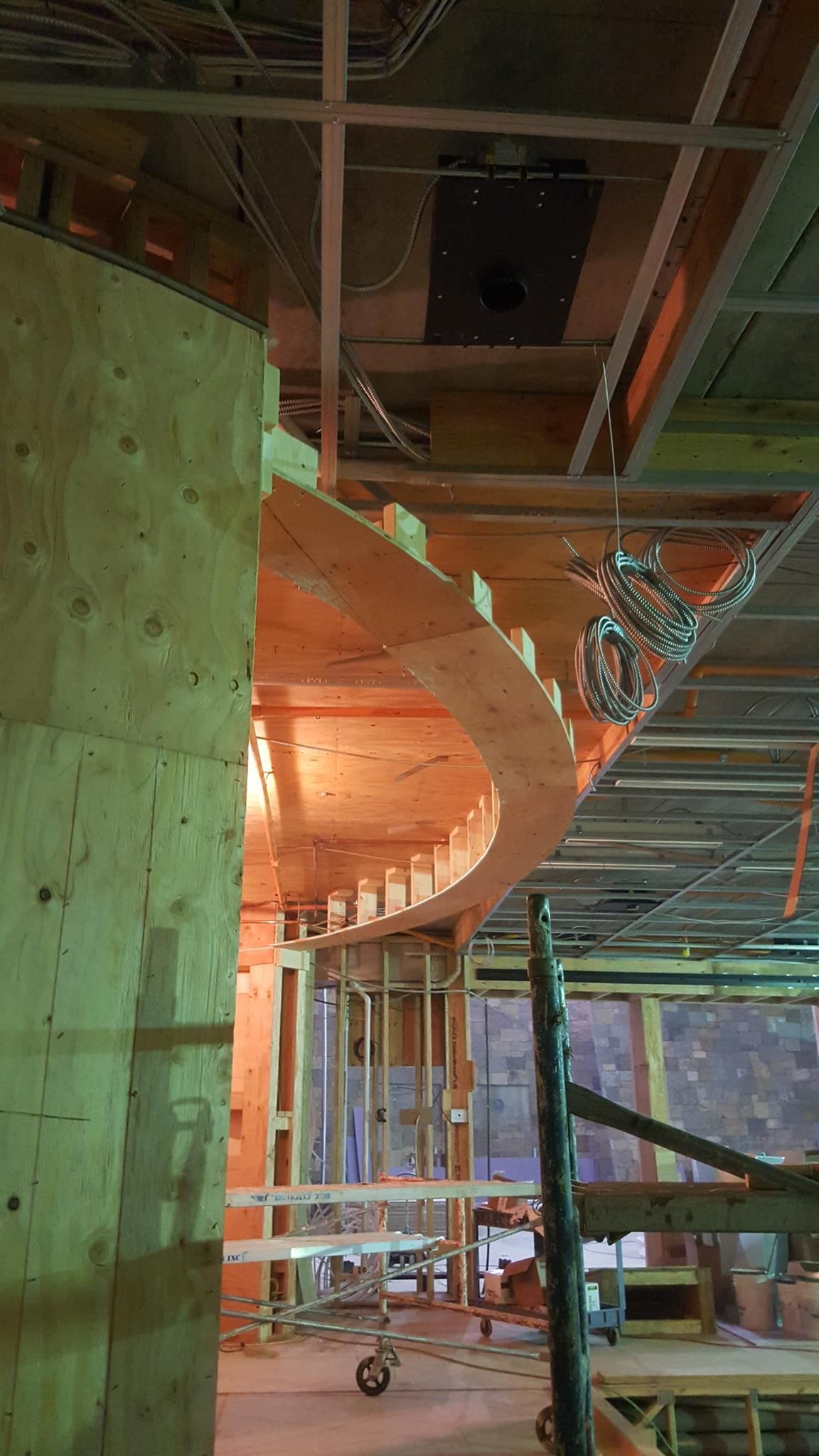 Construction site showing curved wooden wall framing, support beams, and exposed ceiling infrastructure.