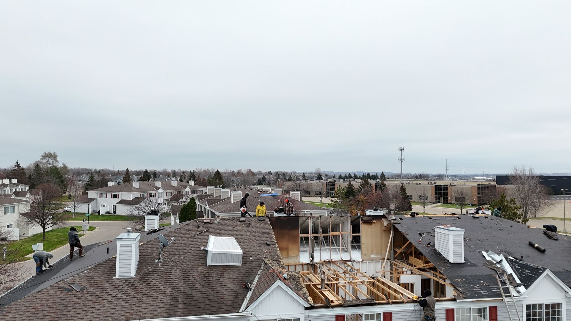 Roofers working on damaged roof in a suburban area under cloudy sky.
