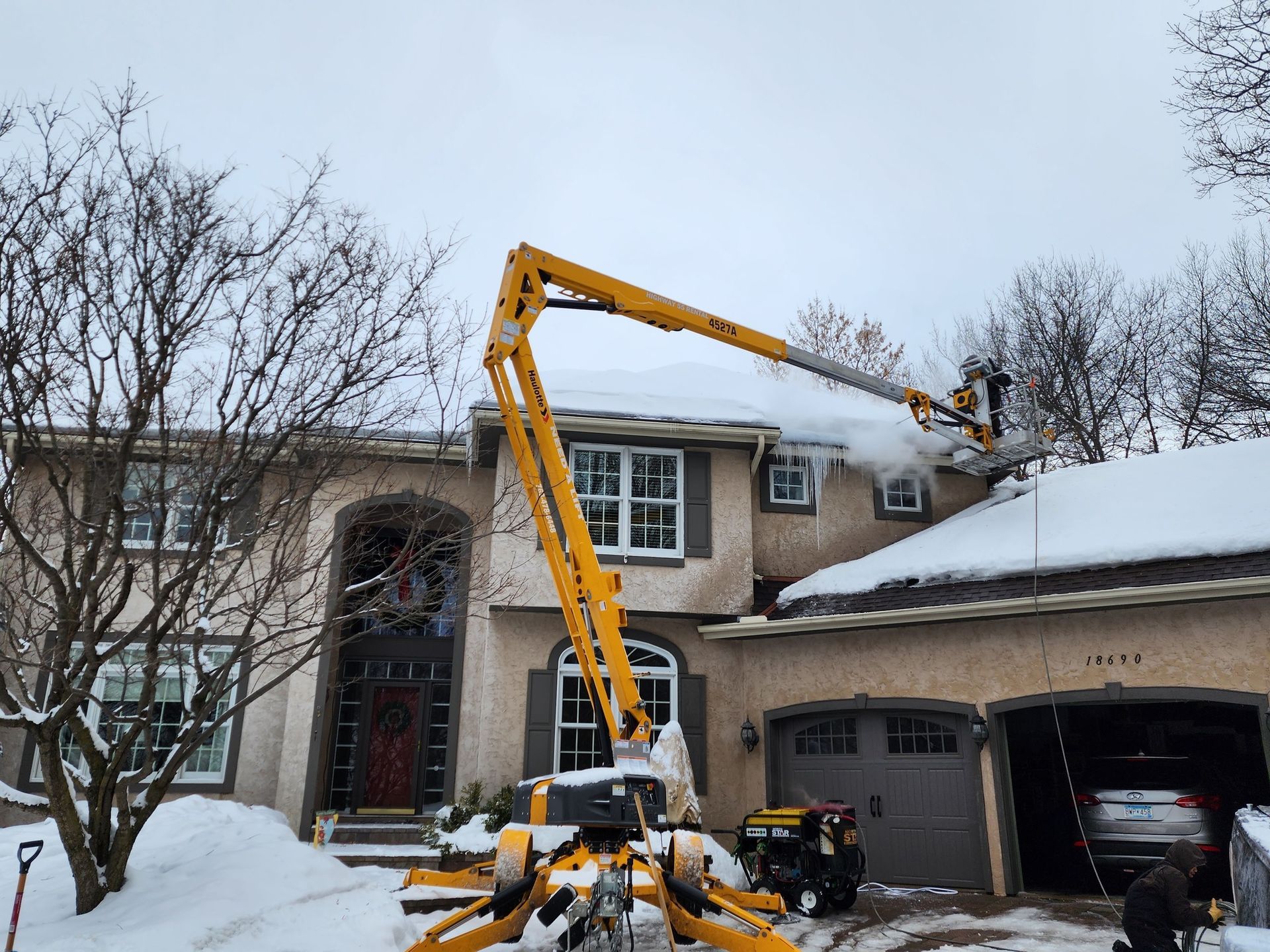 Yellow snow removal machine clearing snow from a house roof on a snowy day.
