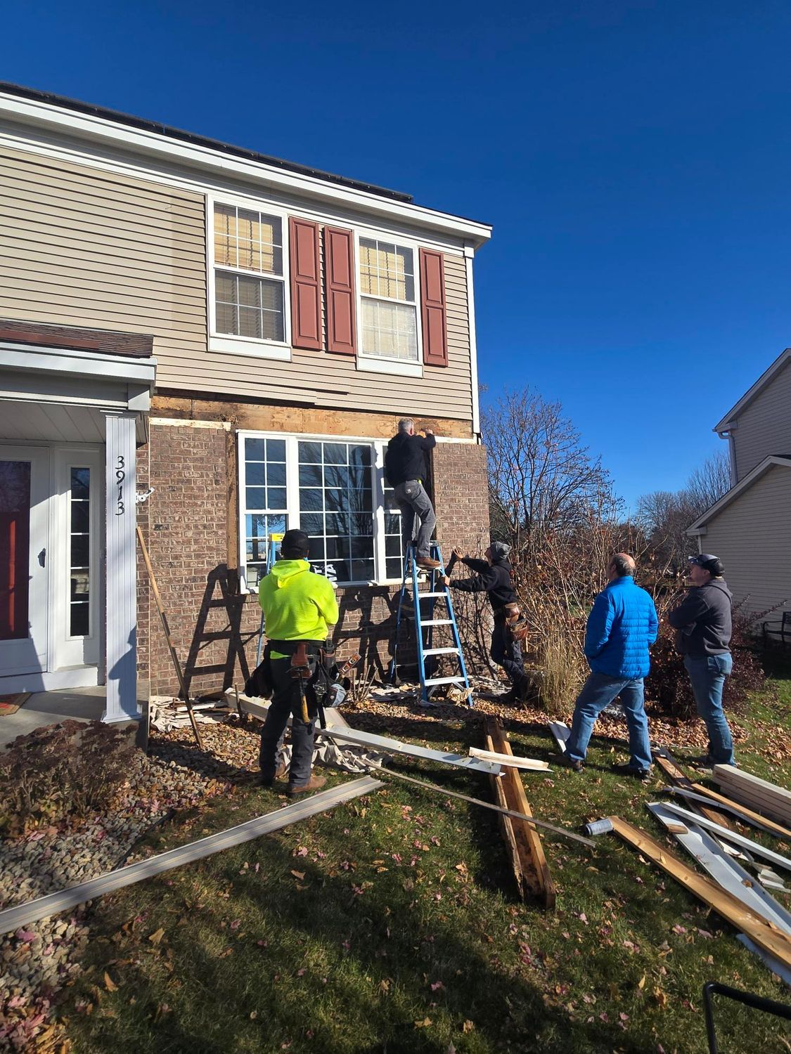 Construction workers on ladders renovating a house exterior, sunny day.