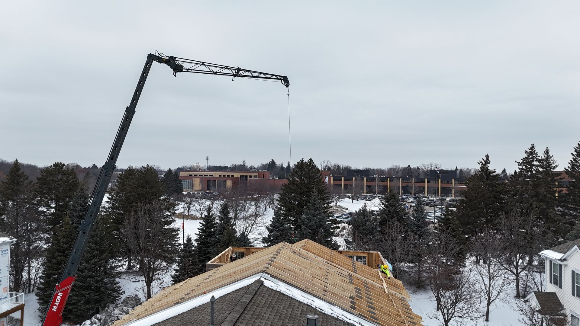 Crane lifting materials onto a partially built house roof in a snowy setting.