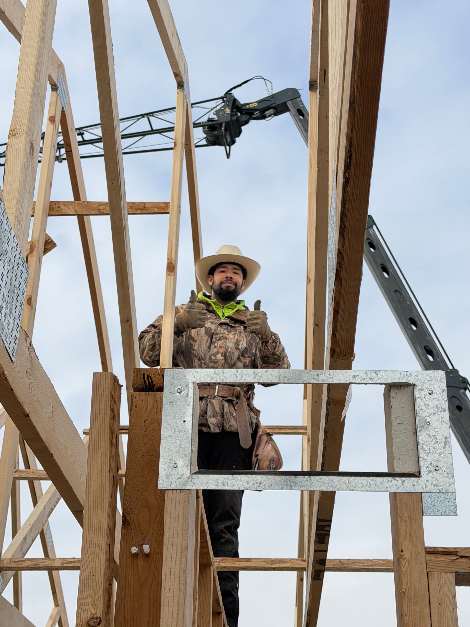 Construction worker in cowboy hat gives thumbs up, standing inside a wooden frame.