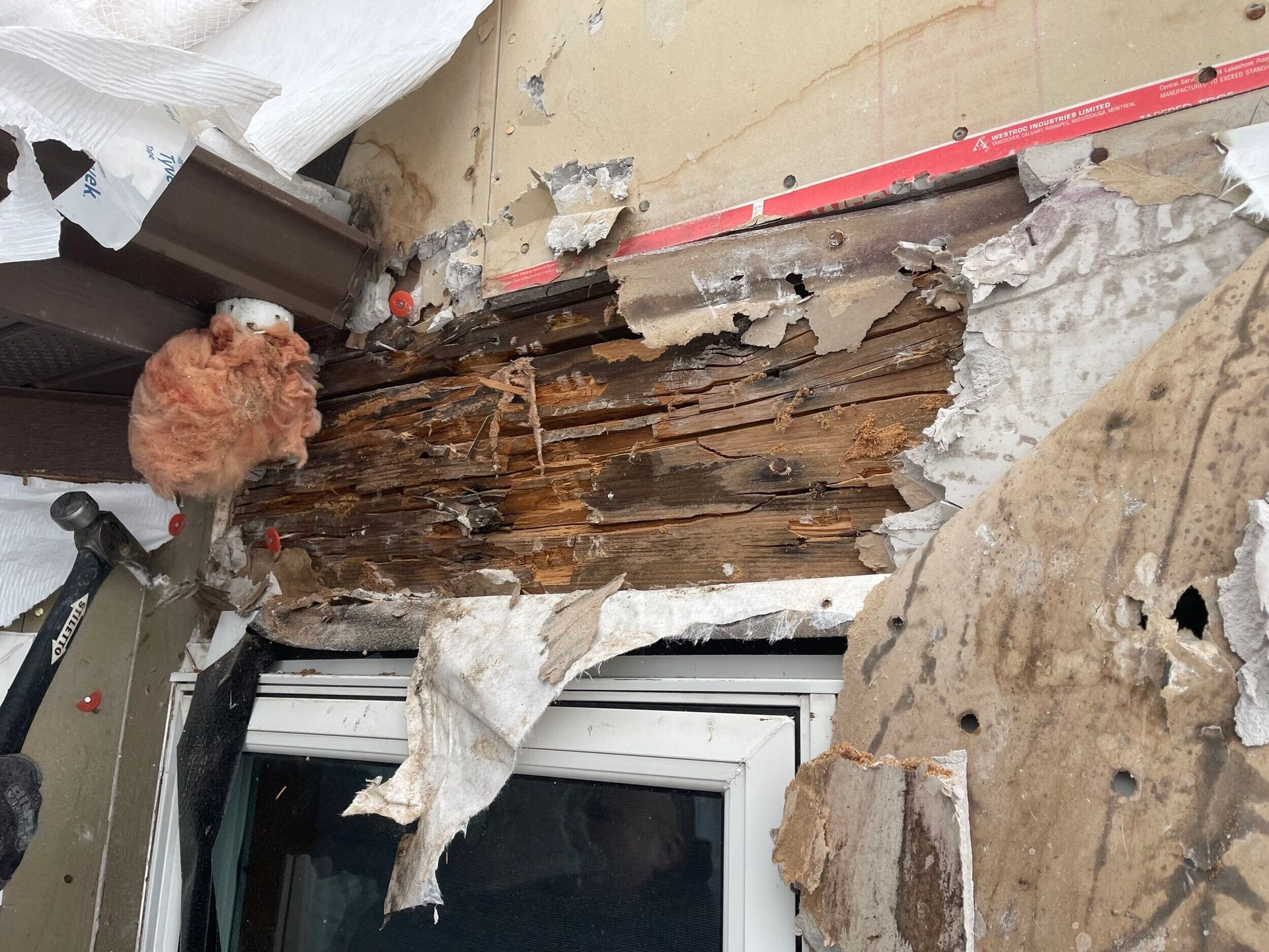 Damaged wooden structure above a window, showing rot and exposed interior.