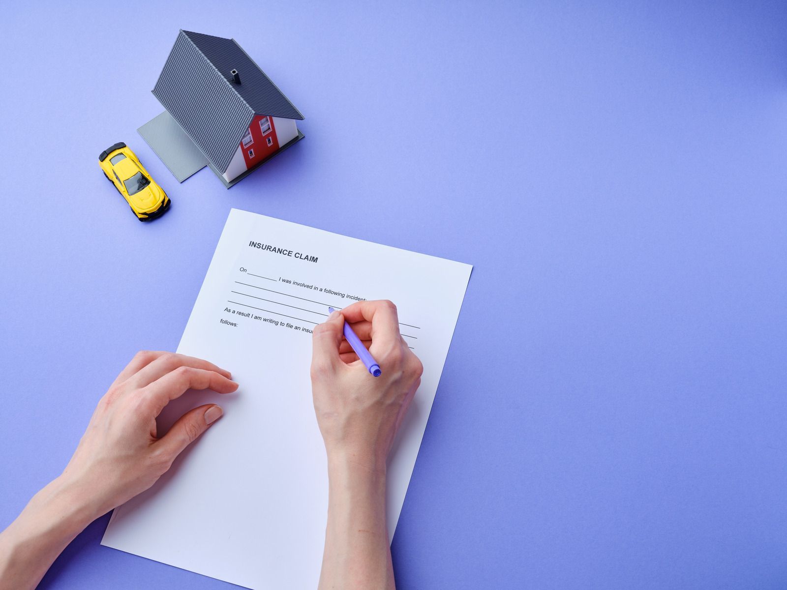 Hands writing on a document with a miniature house and car on a purple background.