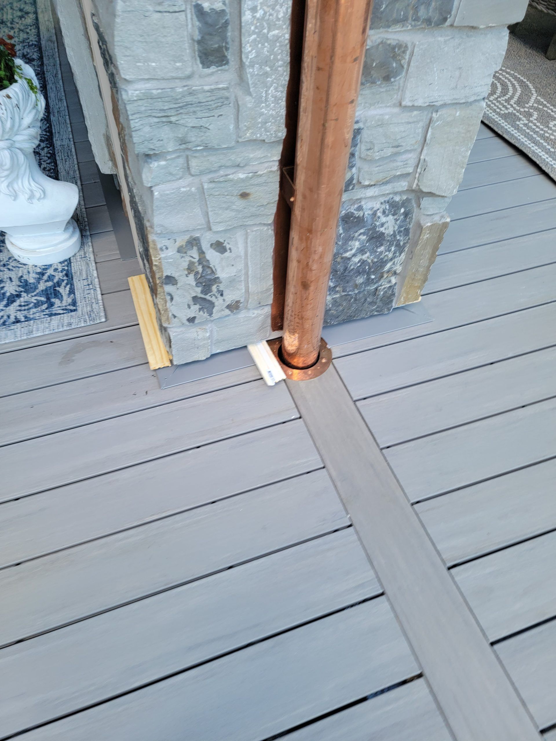 Copper rain gutter alongside stone column on a gray deck.