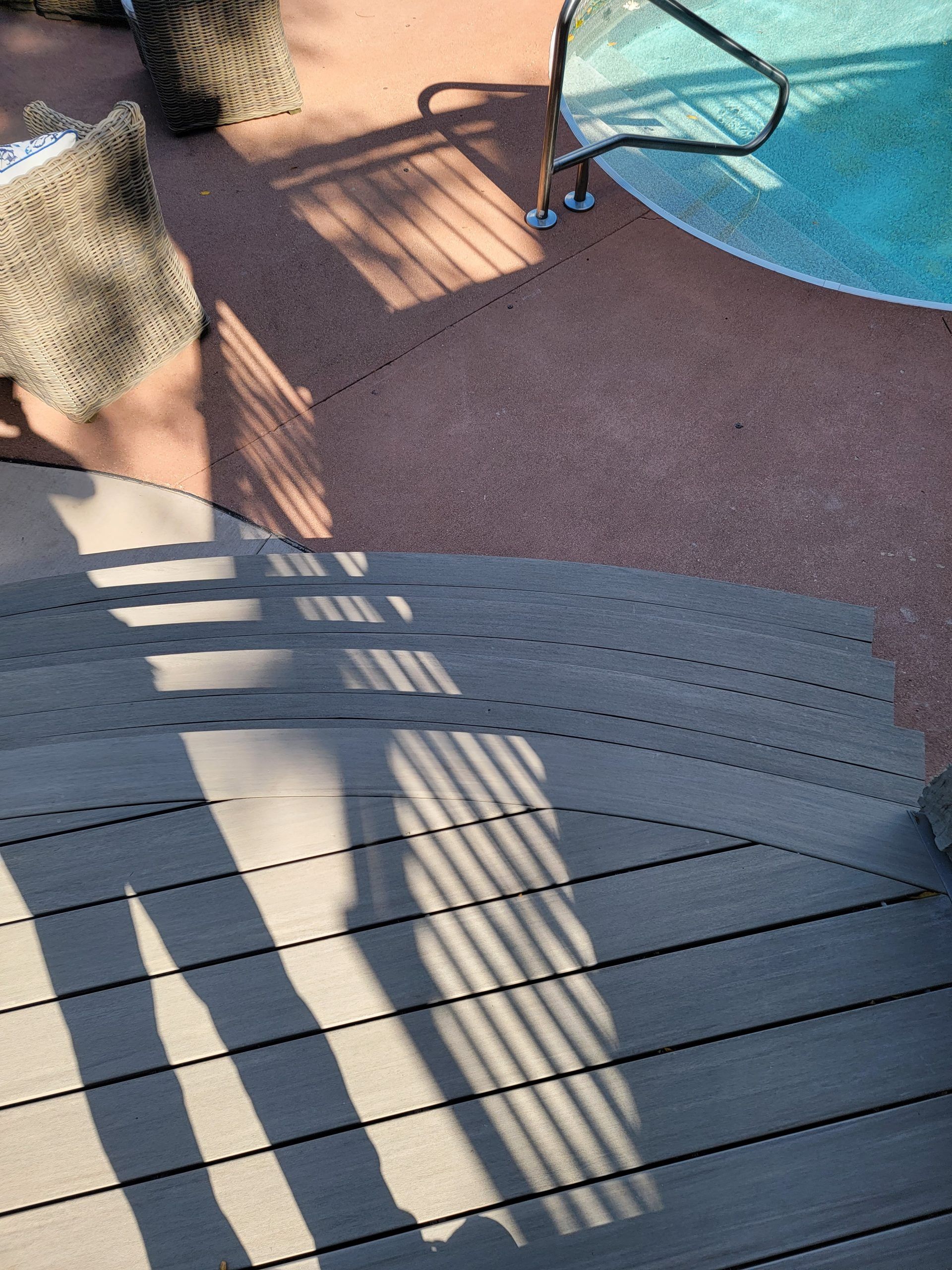 Wooden deck stairs leading to a pool area. Shadows cast by a railing on the deck.