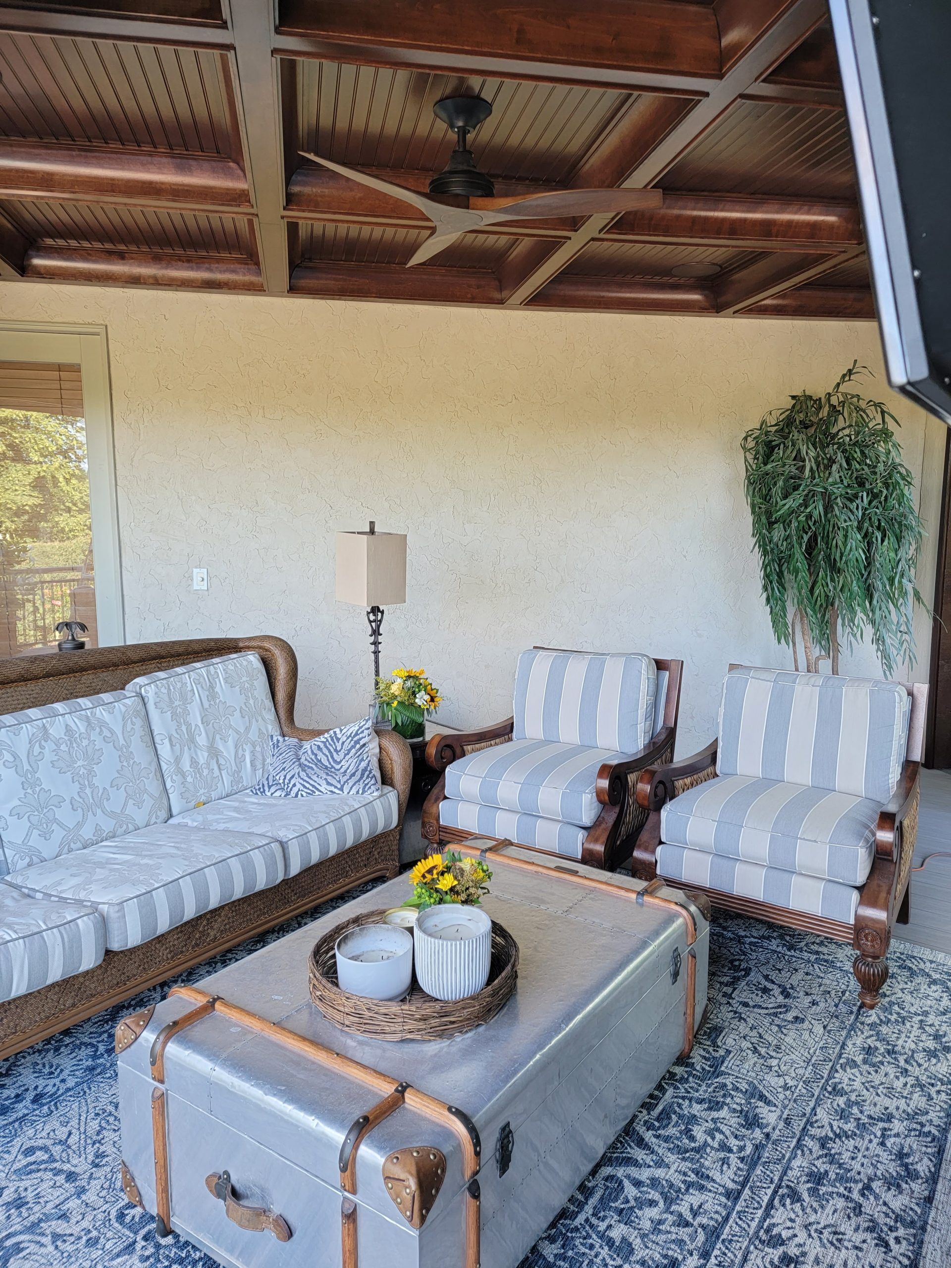 Outdoor seating area with sofa, chairs, and trunk coffee table. Striped cushions, wooden frames, ceiling fan.