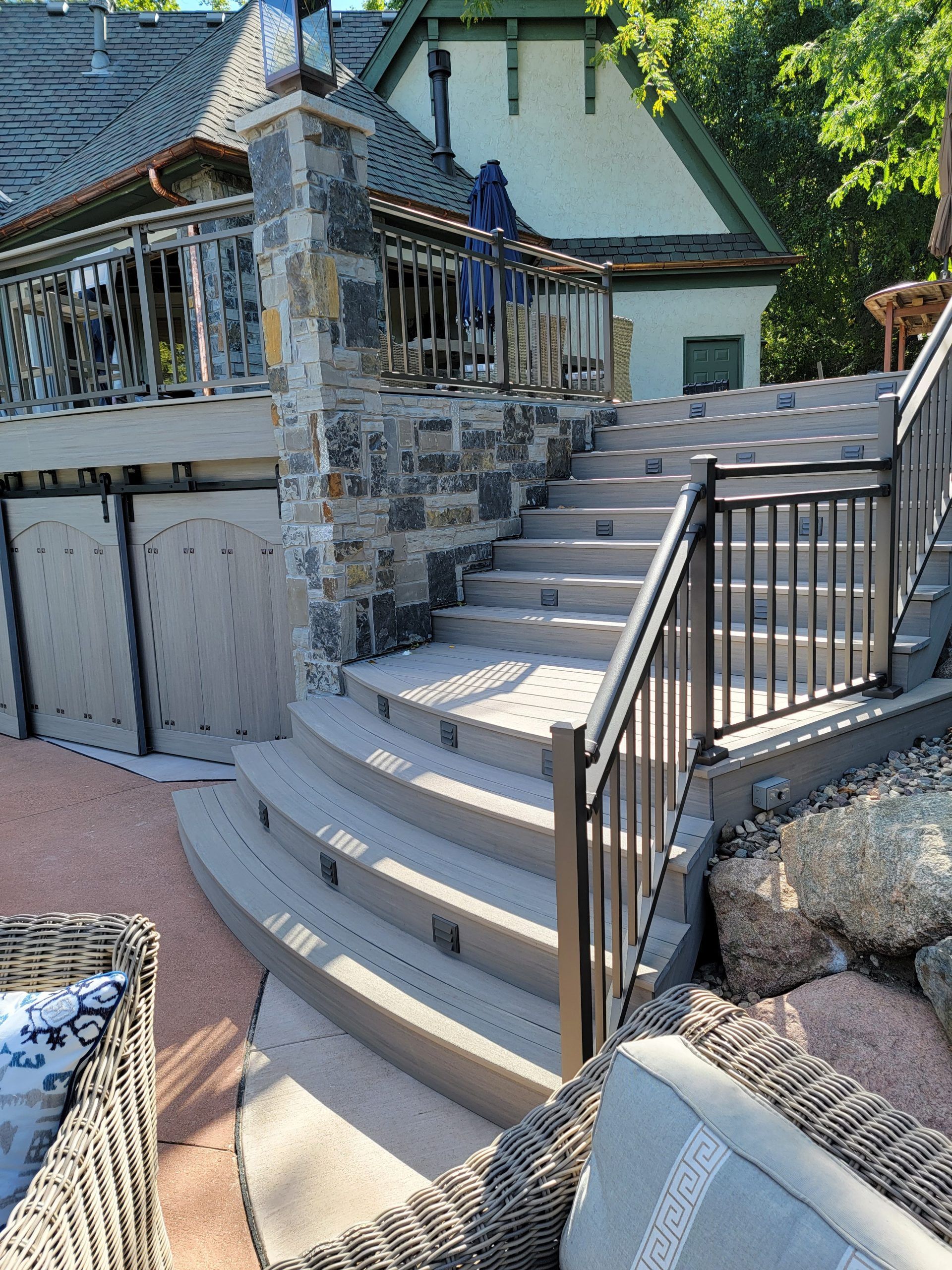 Stone and wood steps lead up to a building with railing. Deck furniture is visible in foreground.