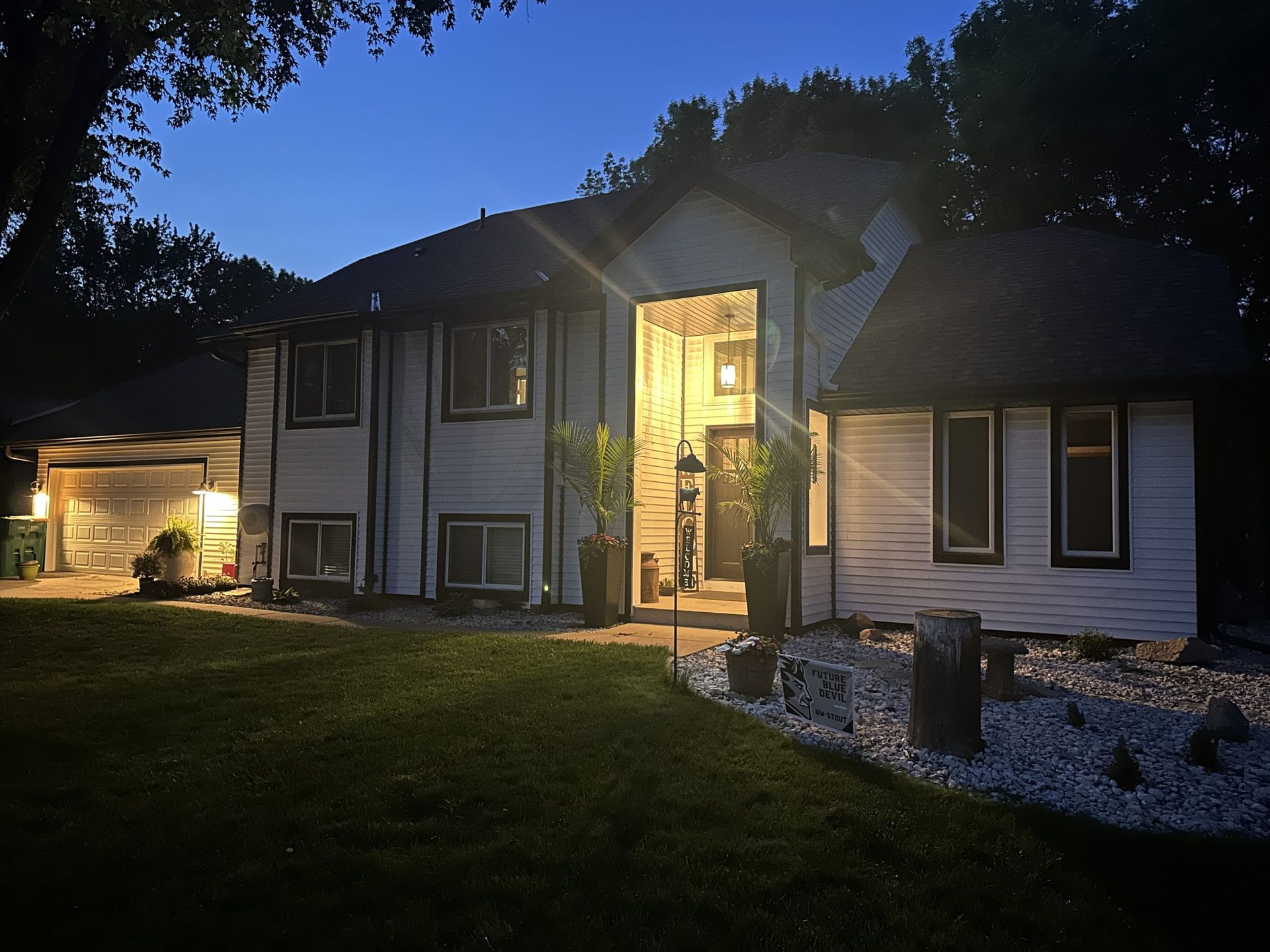 Two-story house at dusk, lit from inside. Garage, front door, and landscaping visible.