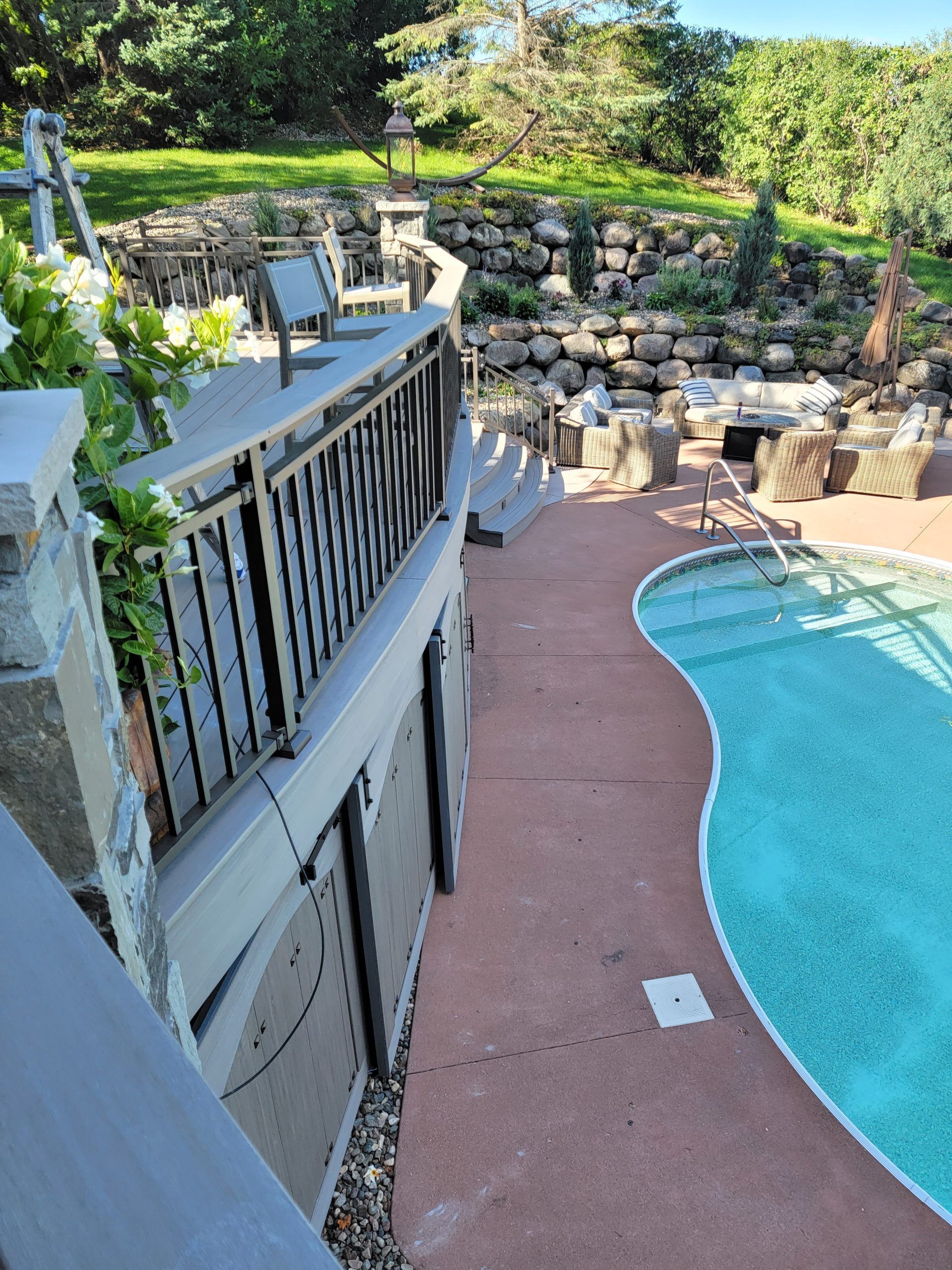 Deck overlooking a pool with a waterfall feature. Gray deck railing and concrete steps.