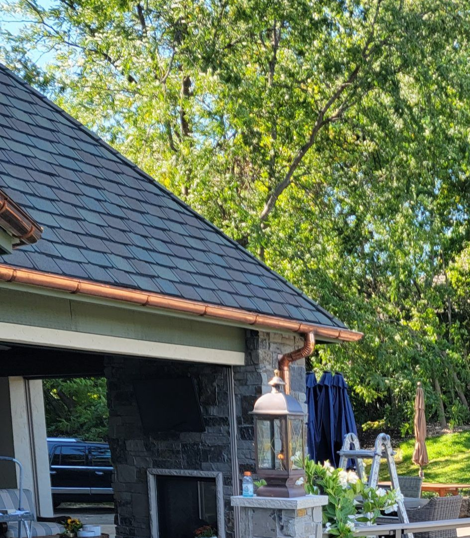 Backyard deck with pool and outdoor seating. Trees and house with stone chimney in the background.