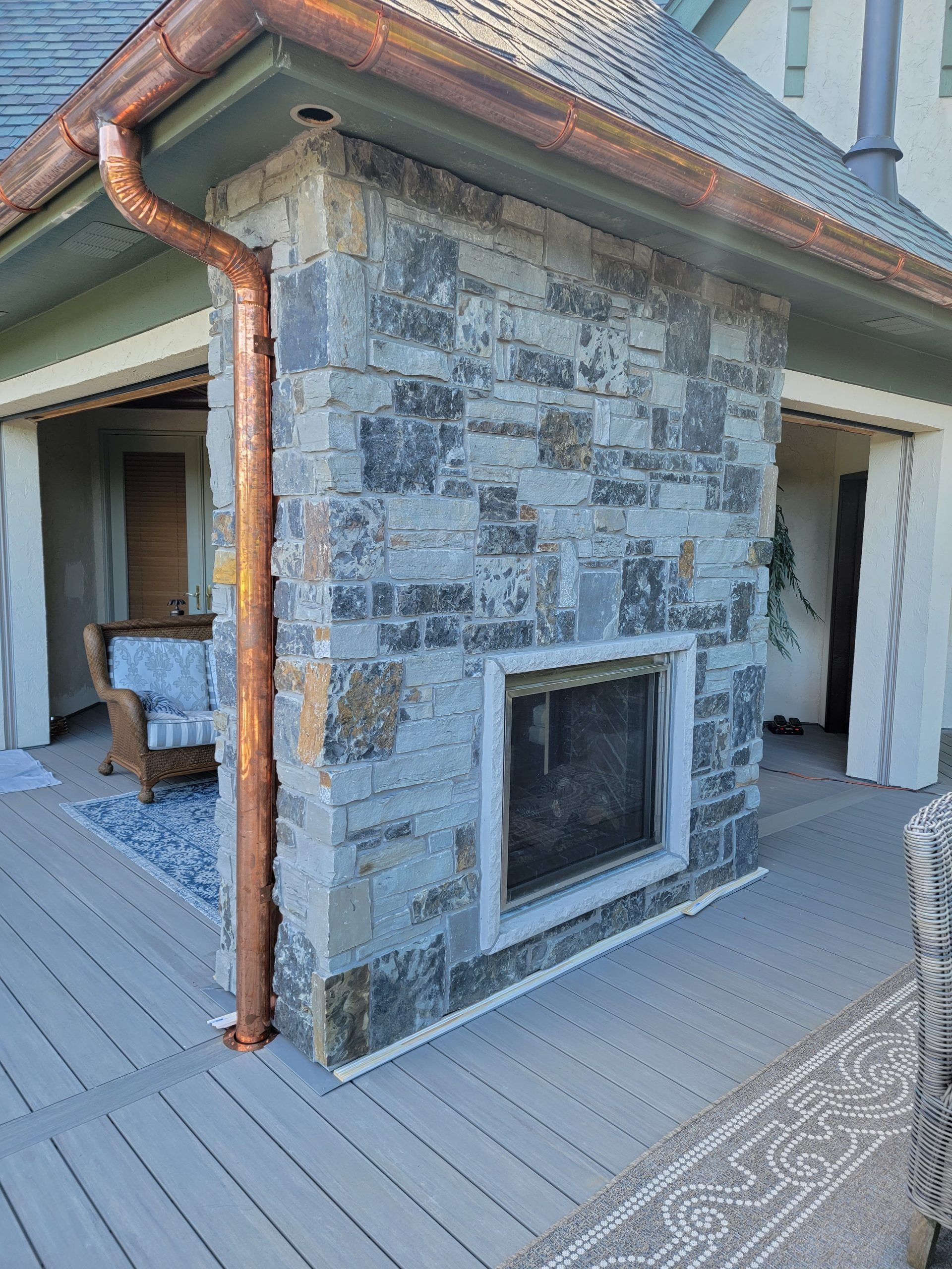 Stone fireplace on a wooden deck, with a copper rain gutter.