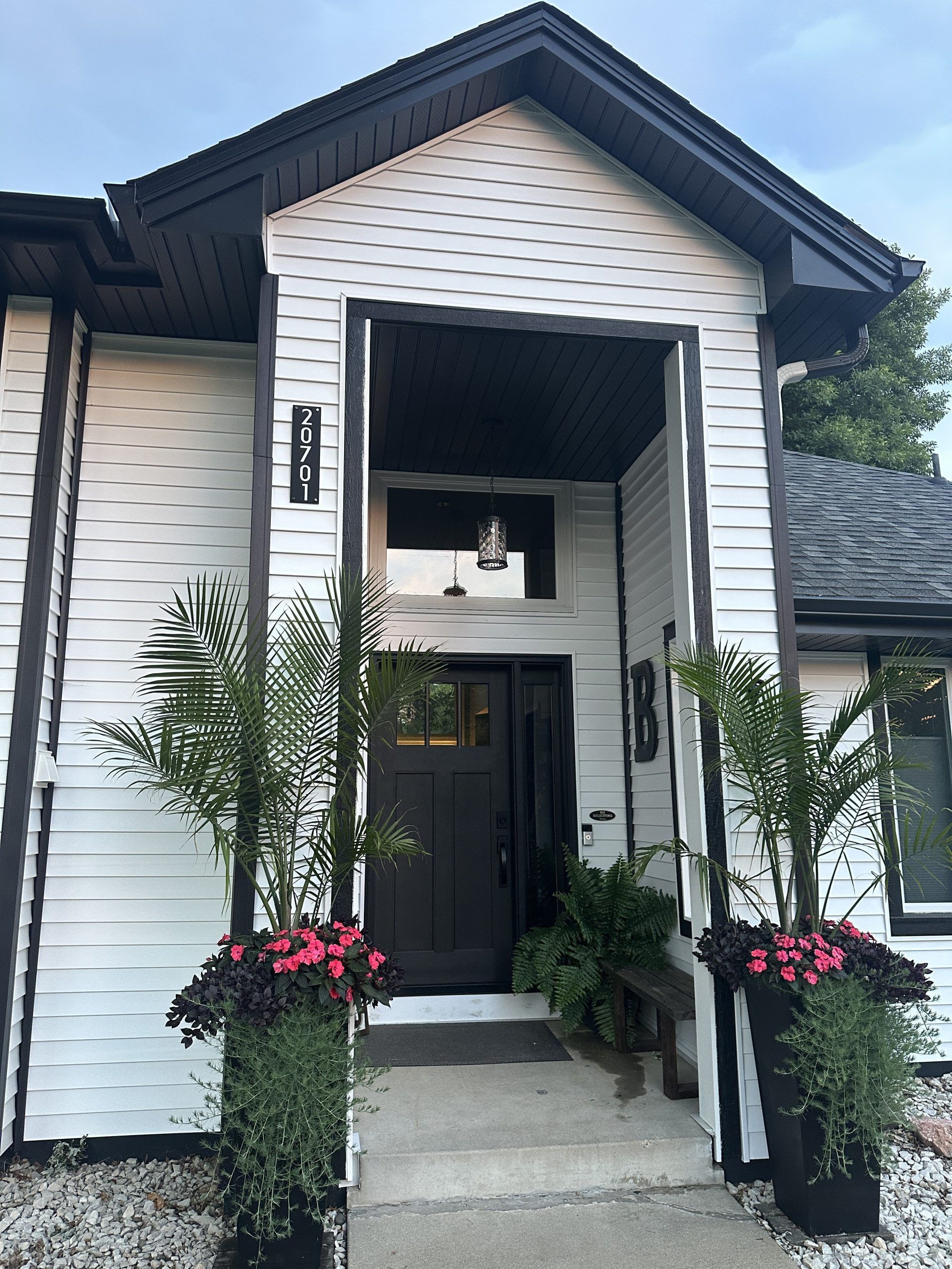 White house entrance with black trim, dark door, and potted plants.