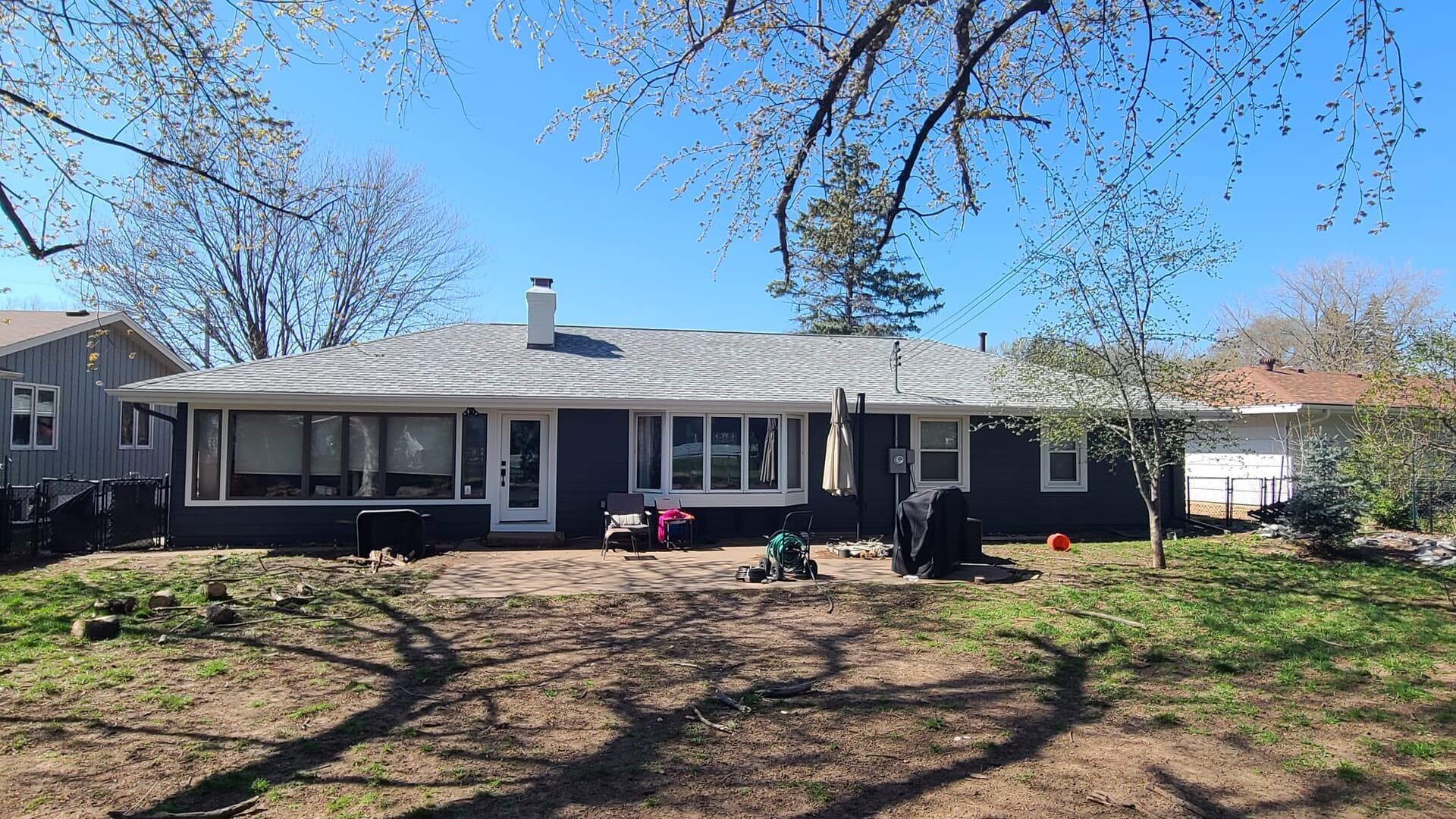 Back view of a dark blue house with white trim, a gray roof, and a tree-lined yard.