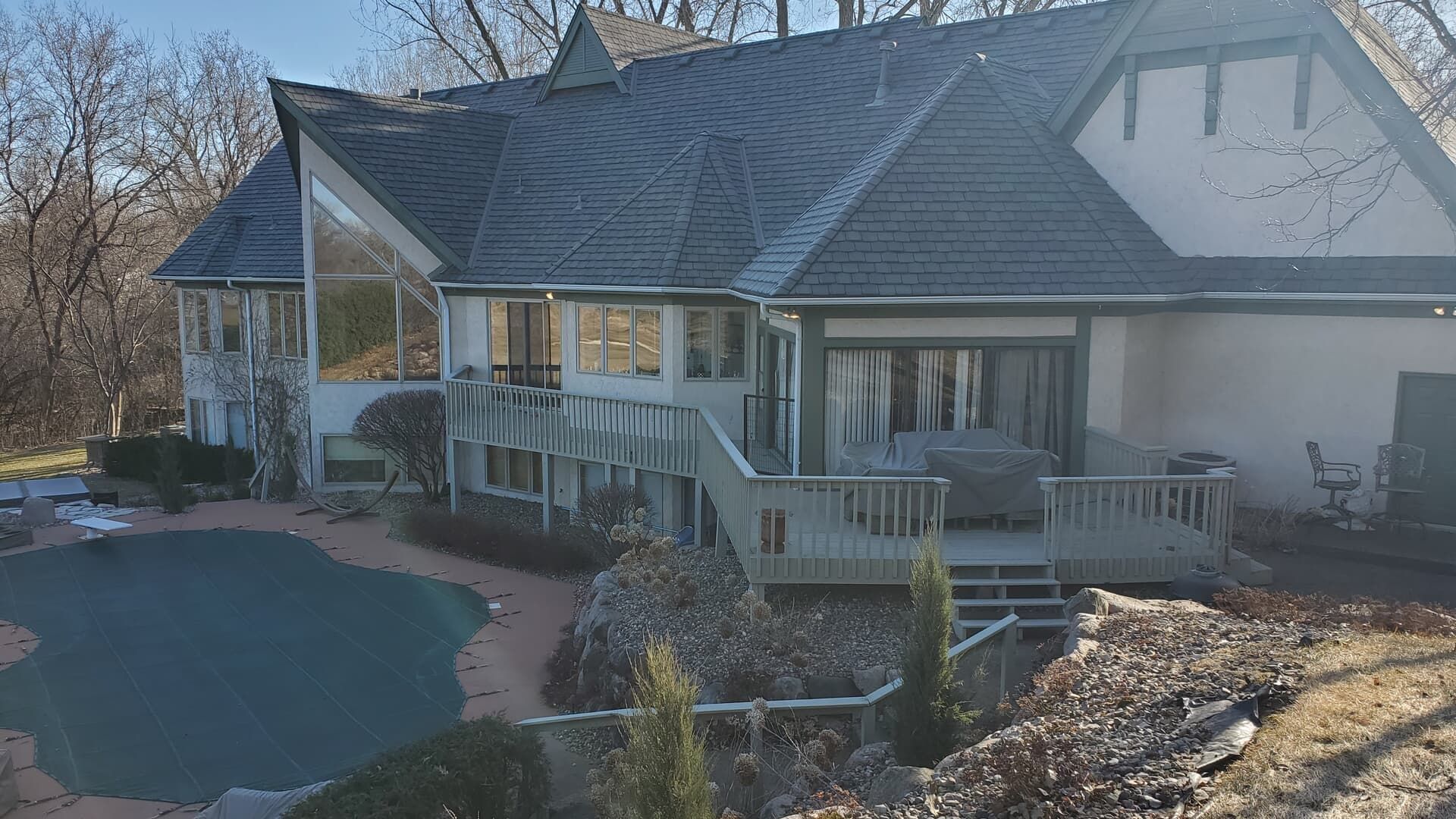 House with gray roof, deck, and pool. Overcast sky.