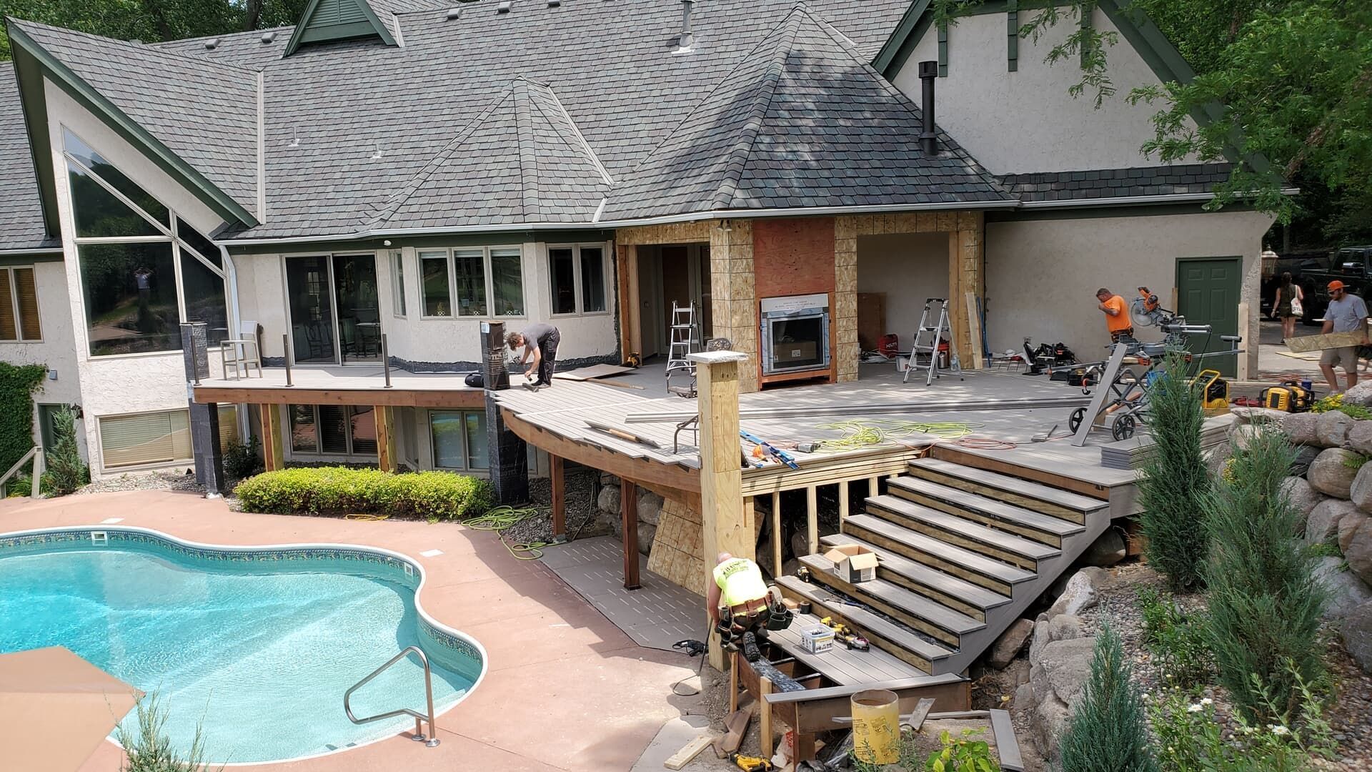 House under construction near a pool, with debris, workers, and a partly destroyed deck.