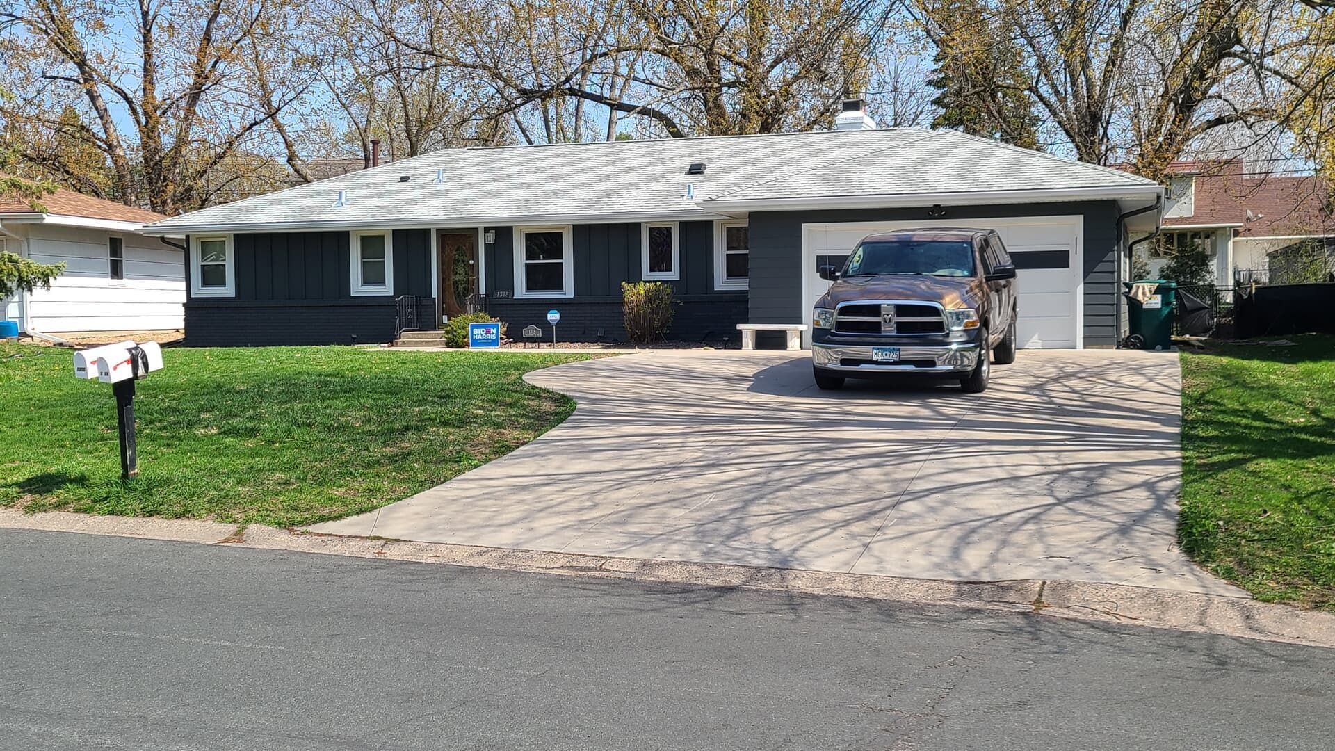Gray house with a driveway and a parked pickup truck. Green grass and trees visible.