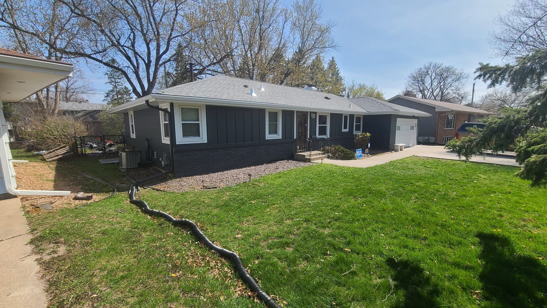 A dark gray house with white trim, green lawn, and a gray roof on a sunny day.