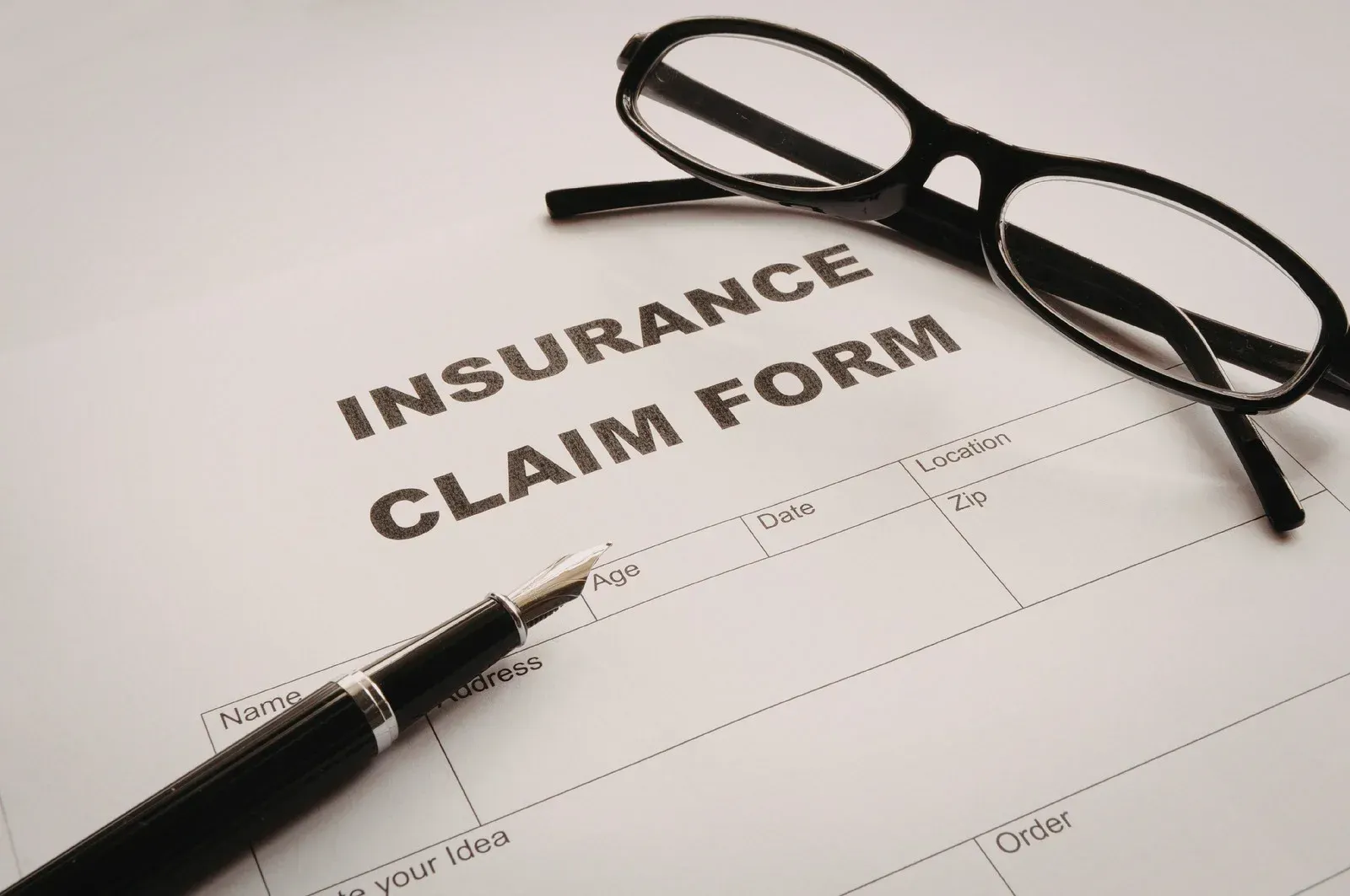 Insurance claim form, eyeglasses, and pen on white paper.