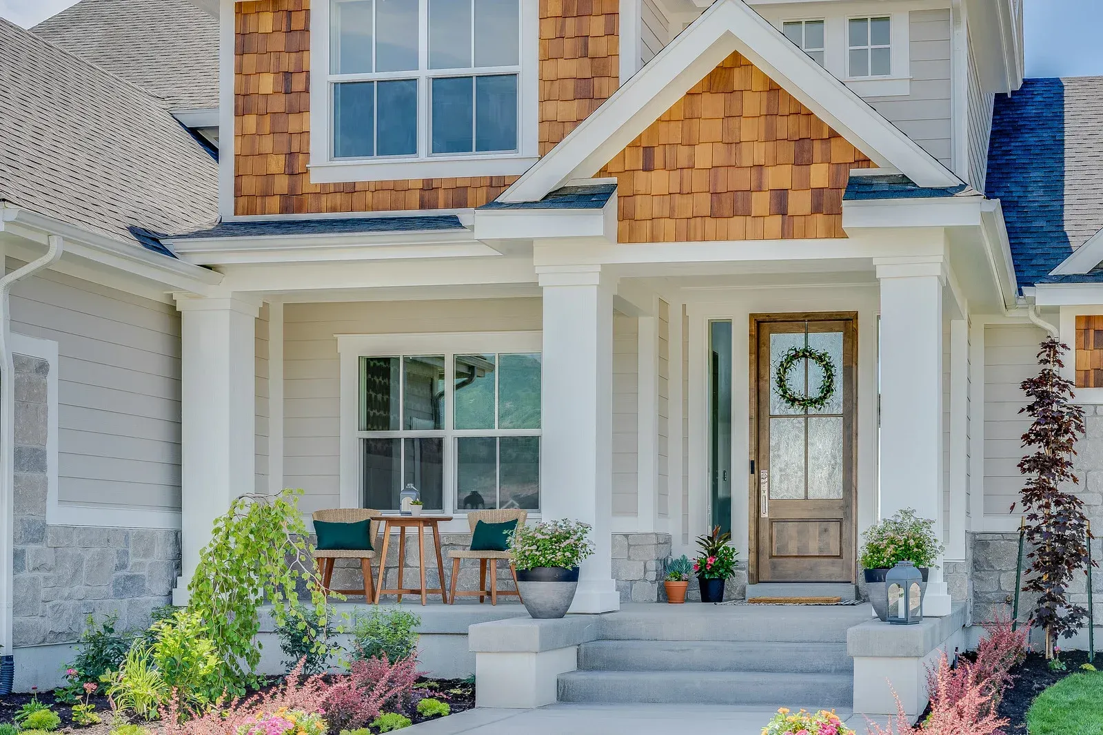 Beige and brown house exterior with a porch, front door with wreath, and landscaping.