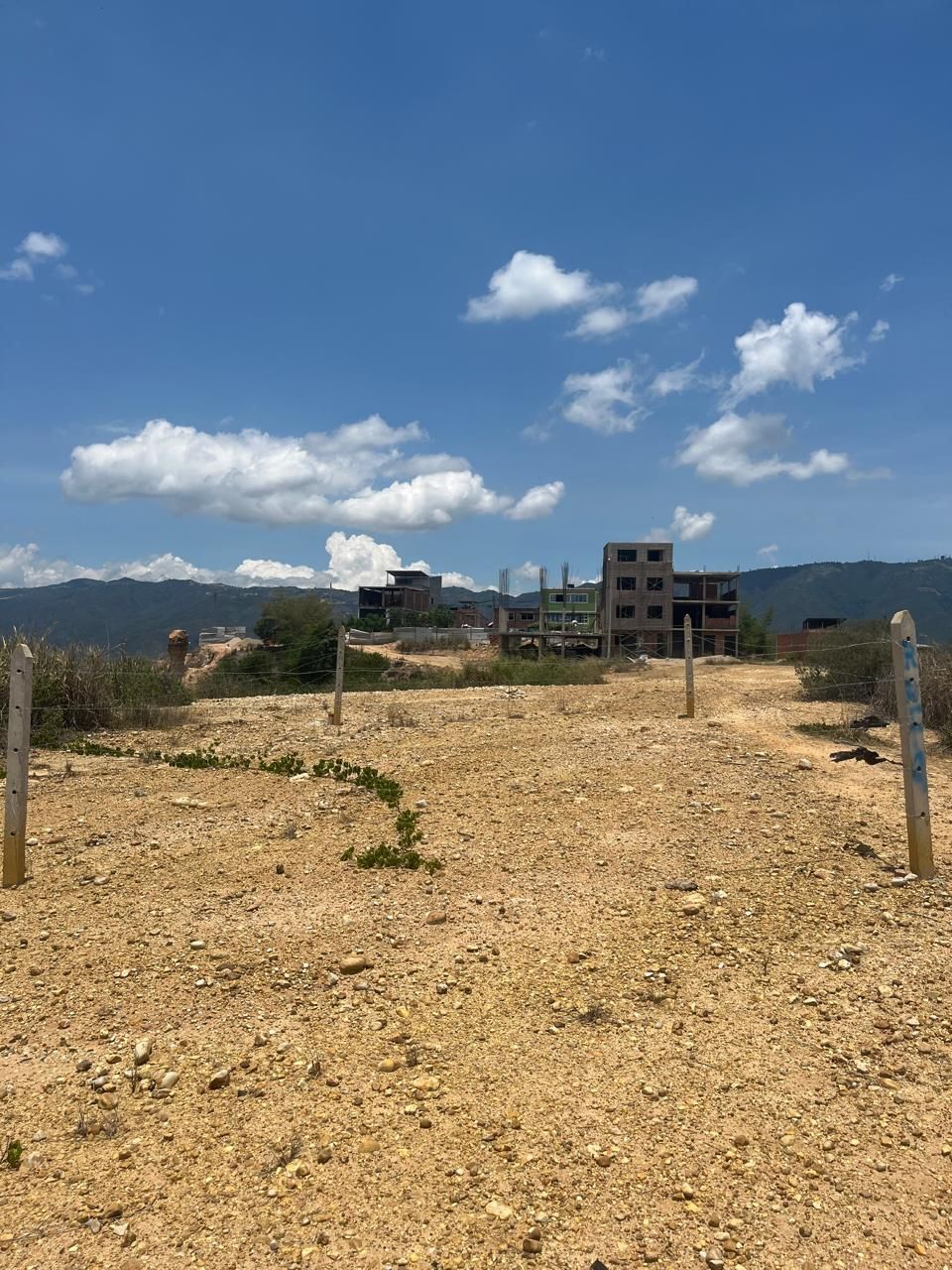 Un campo de tierra con un edificio al fondo y un cielo azul con nubes.