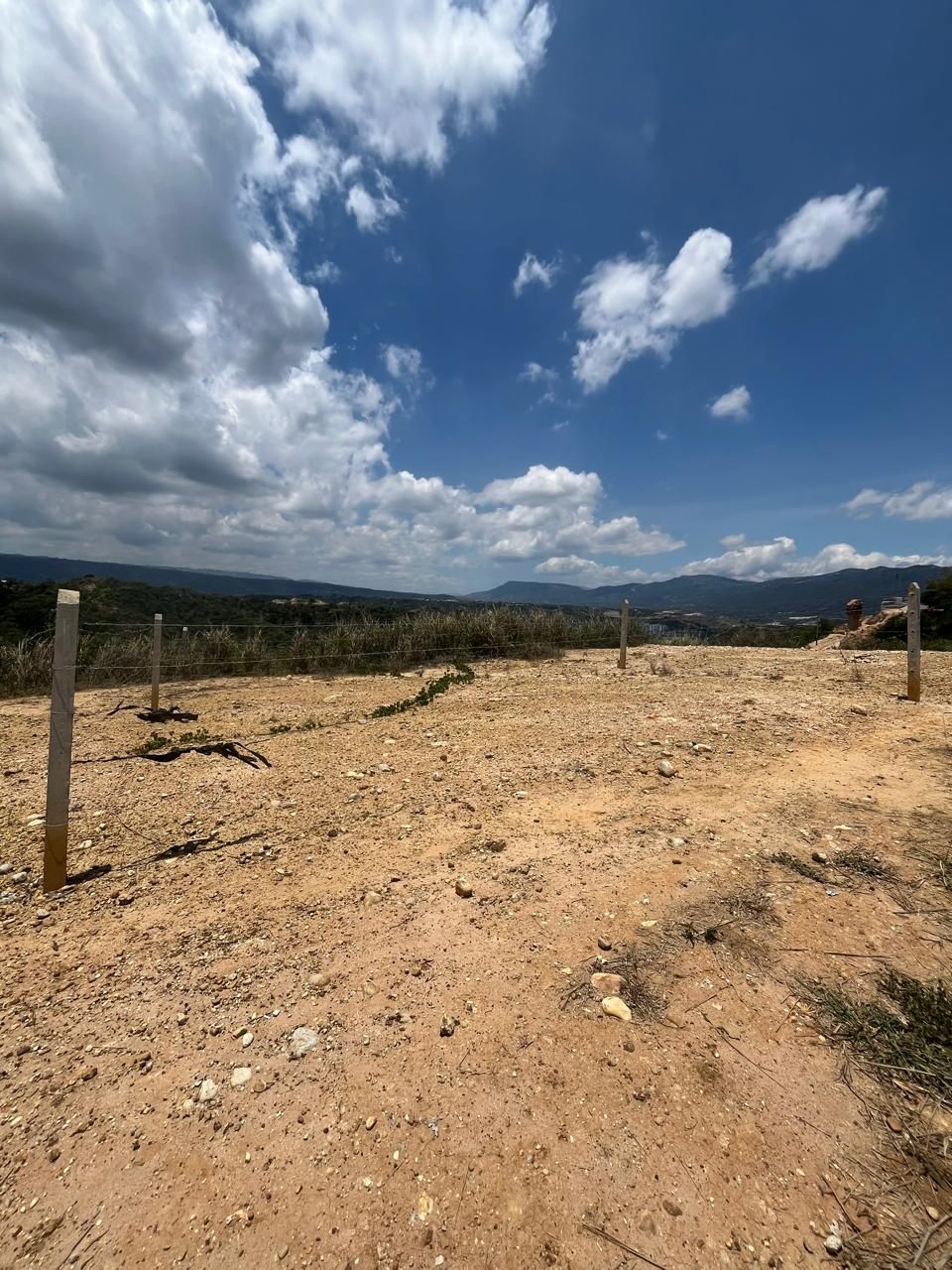 Un campo de tierra con un cielo azul y nubes al fondo.