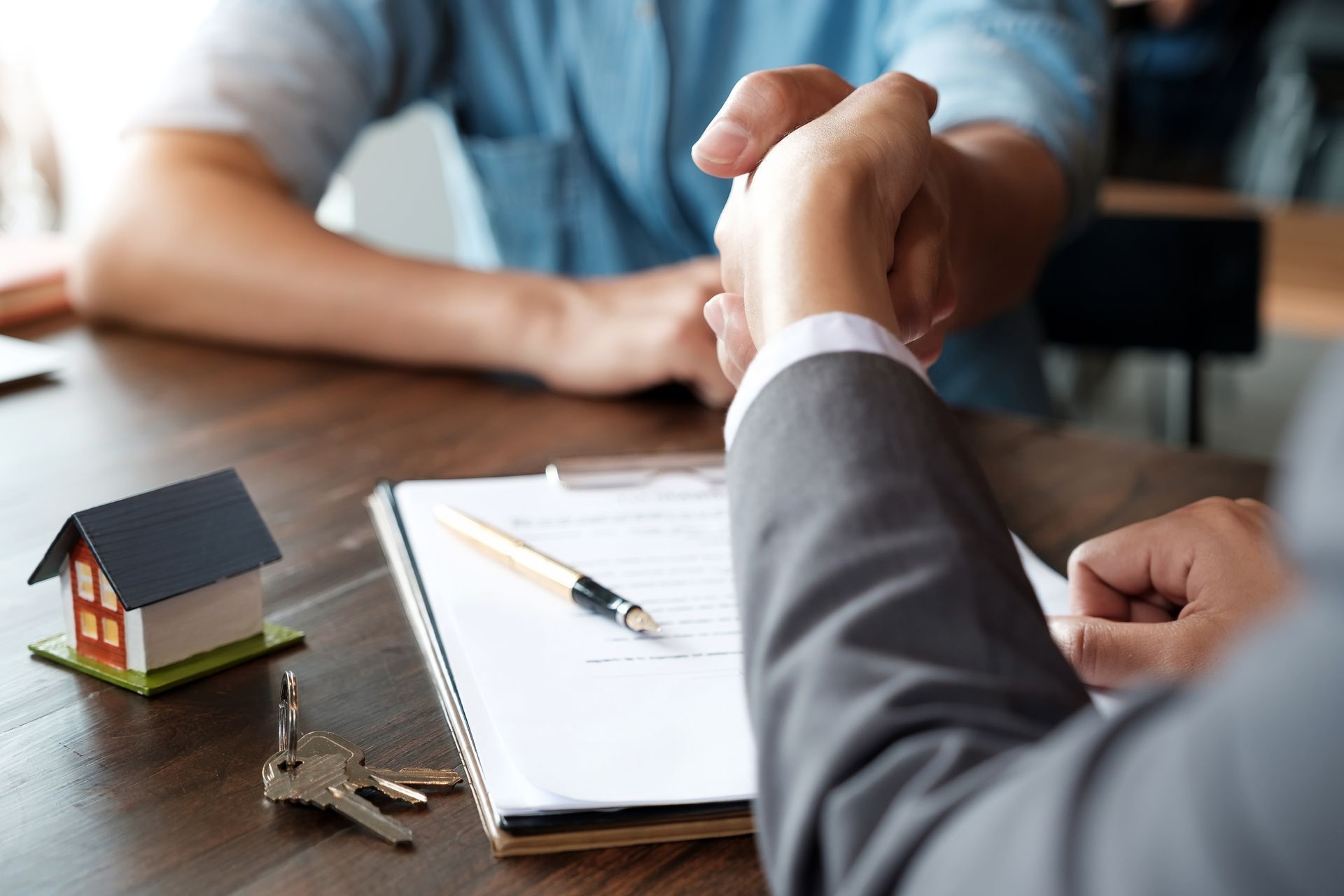 Un hombre le estrecha la mano a un agente inmobiliario mientras está sentado en una mesa.