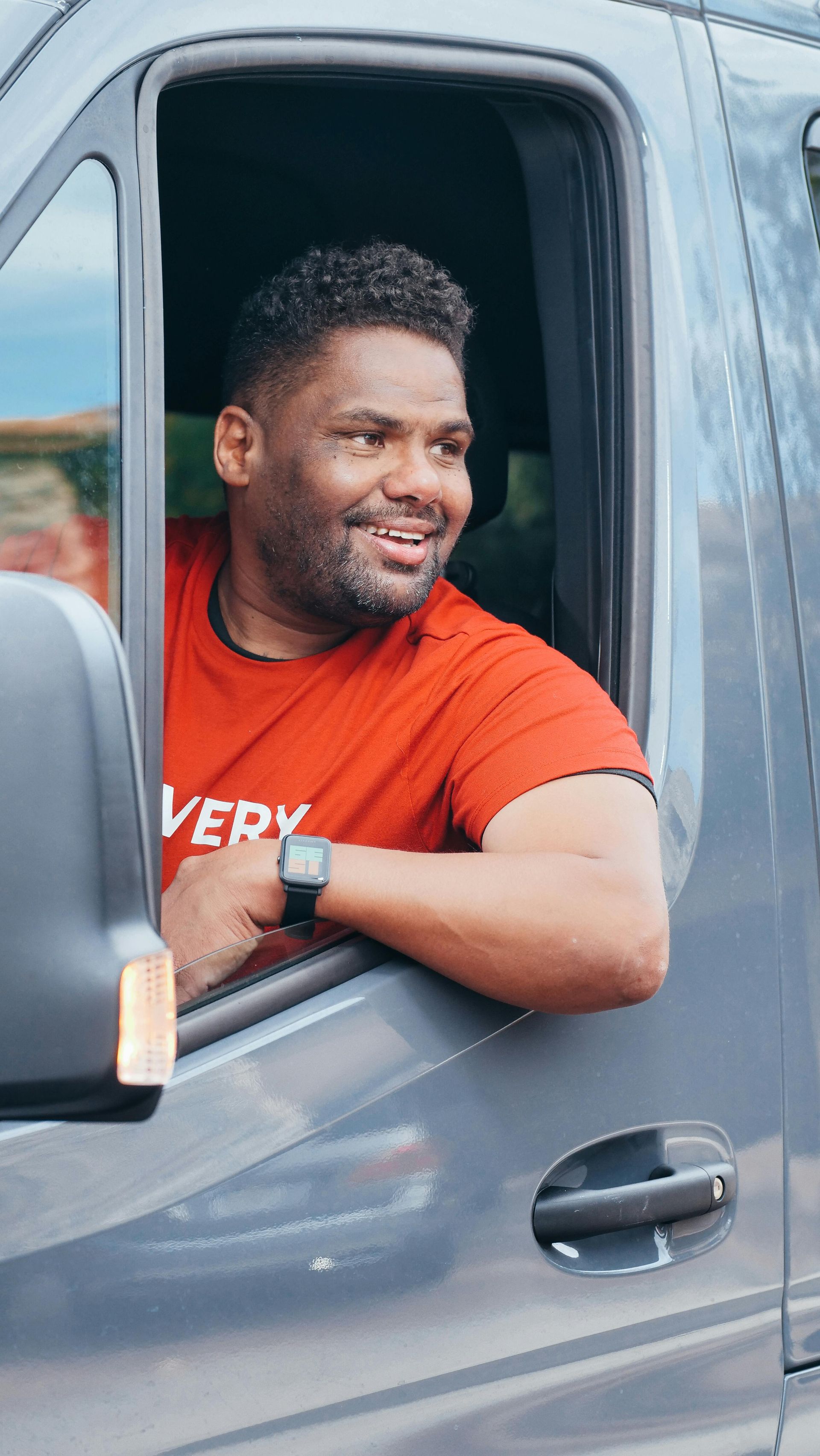 Man in red shirt smiles from delivery van window.