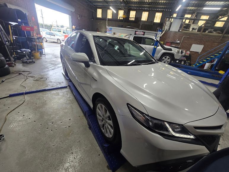 A White Car Is Sitting On A Lift In A Garage — Nuron Inspection & Service Centre In Broadmeadow, NSW