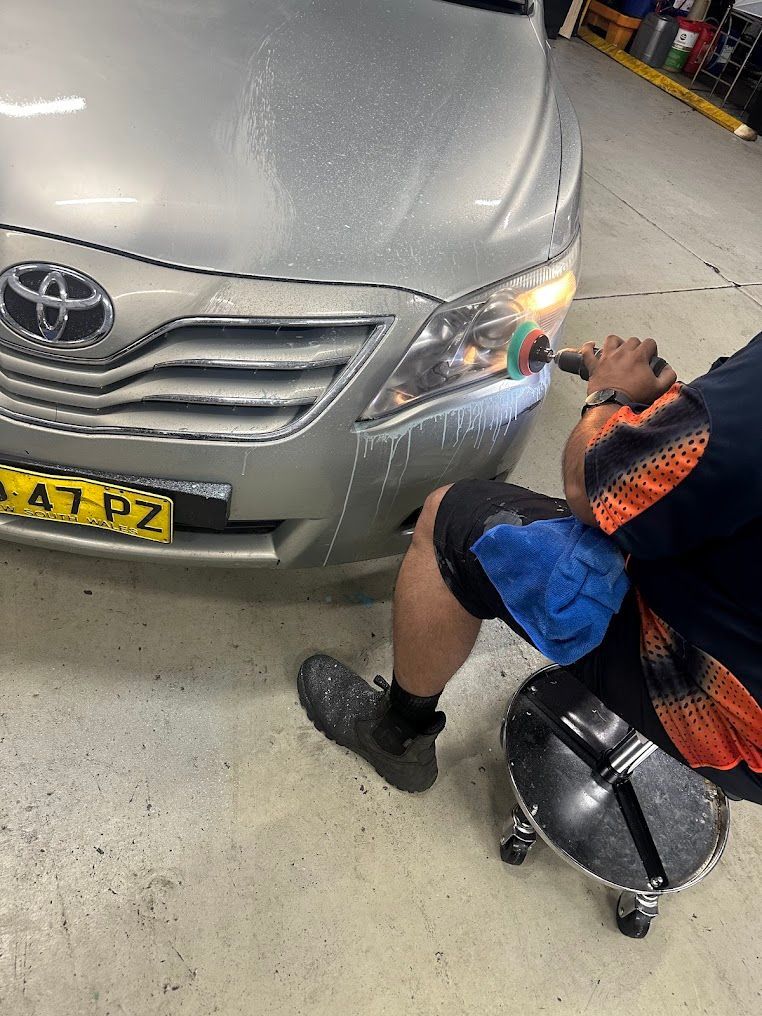 A Man Is Sitting On A Stool Polishing The Headlights Of A Car — Nuron Inspection & Service Centre In Broadmeadow, NSW