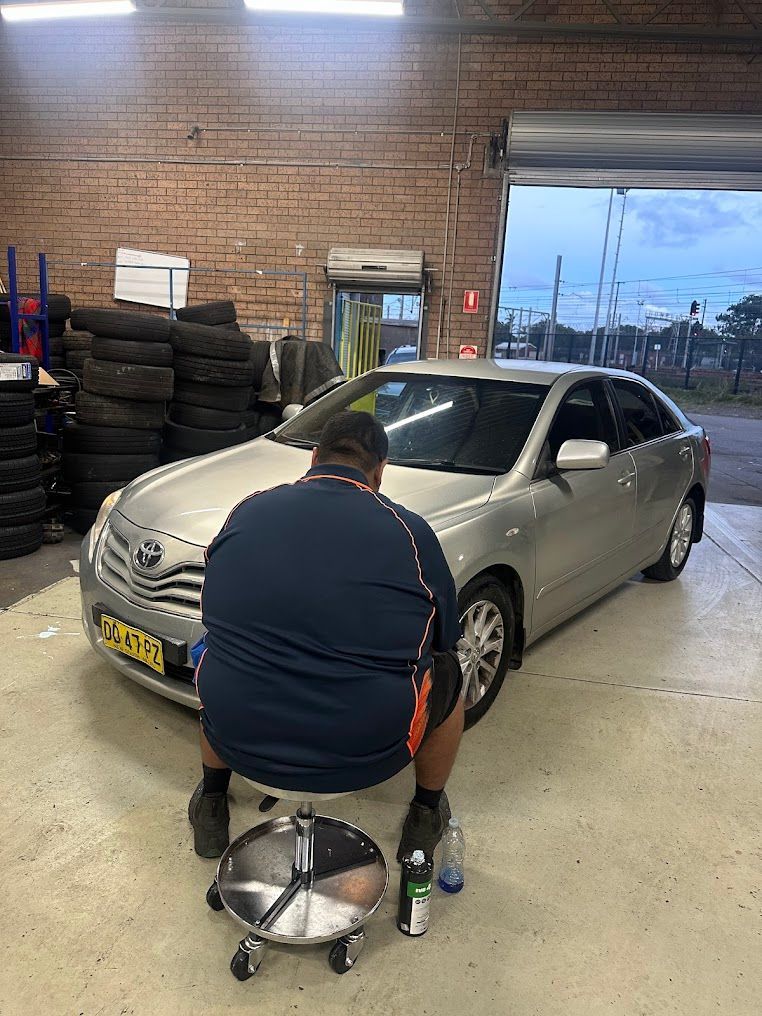 A Man Is Sitting In Front Of A Silver Car In A Garage — Nuron Inspection & Service Centre In Broadmeadow, NSW
