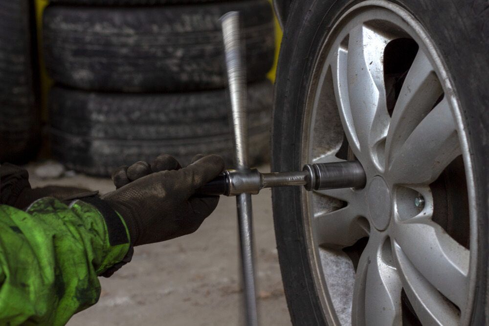 A Person Is Changing A Tire On A Car With A Wrench — Nuron Inspection & Service Centre In Broadmeadow, NSW